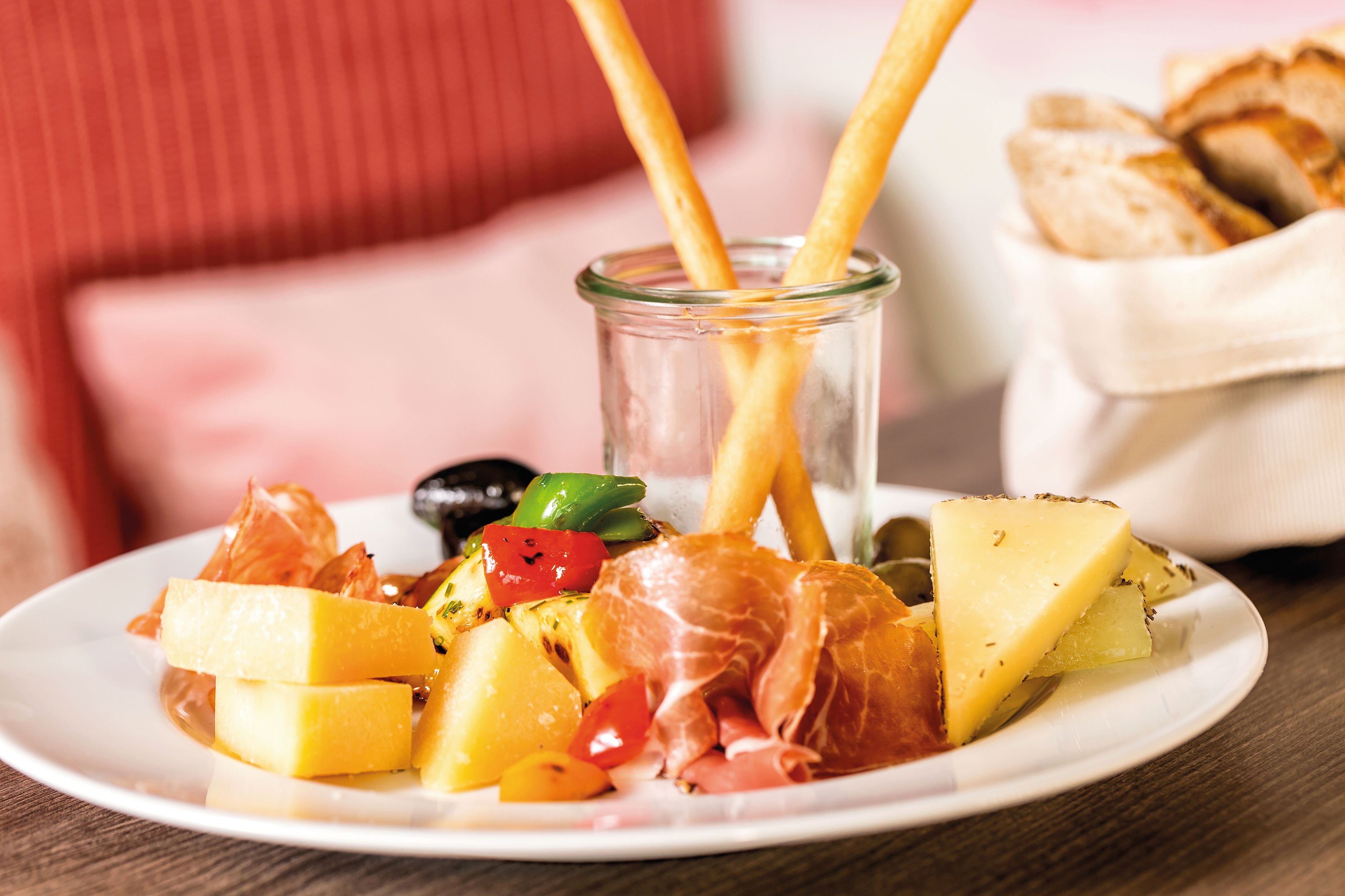 Käse, Schinken, Oliven und Brotstangen auf weißem Teller.