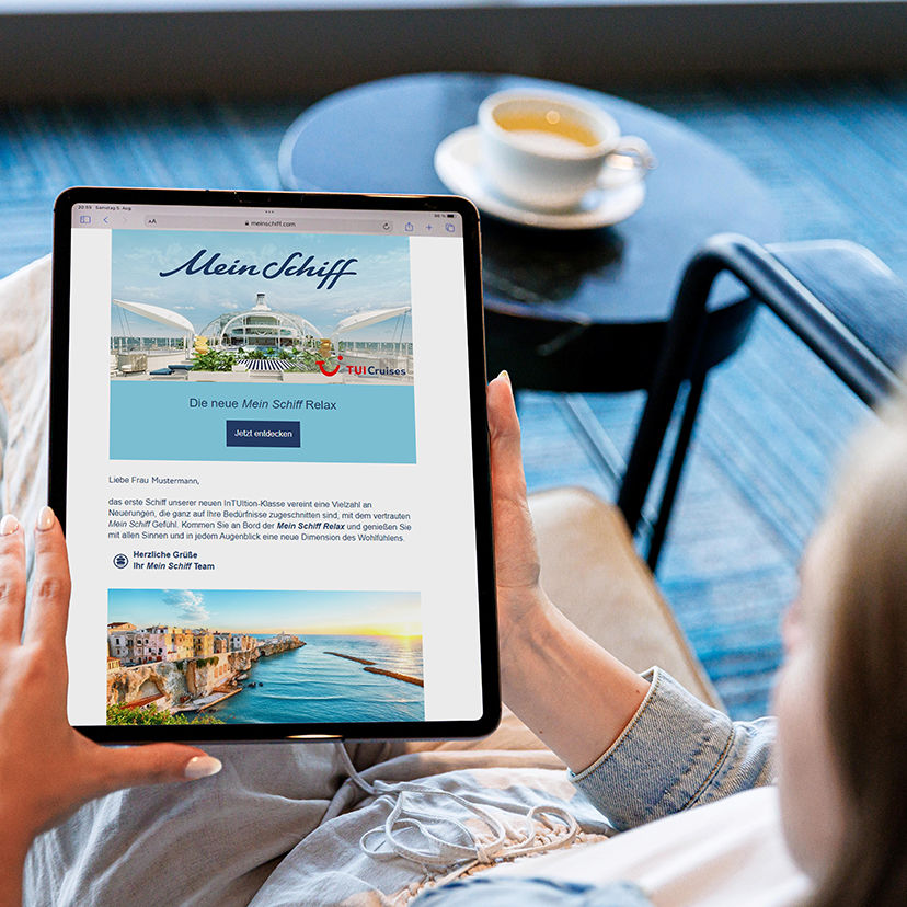 Person hält Tablet mit Mein Schiff Werbung, Tasse Kaffee.