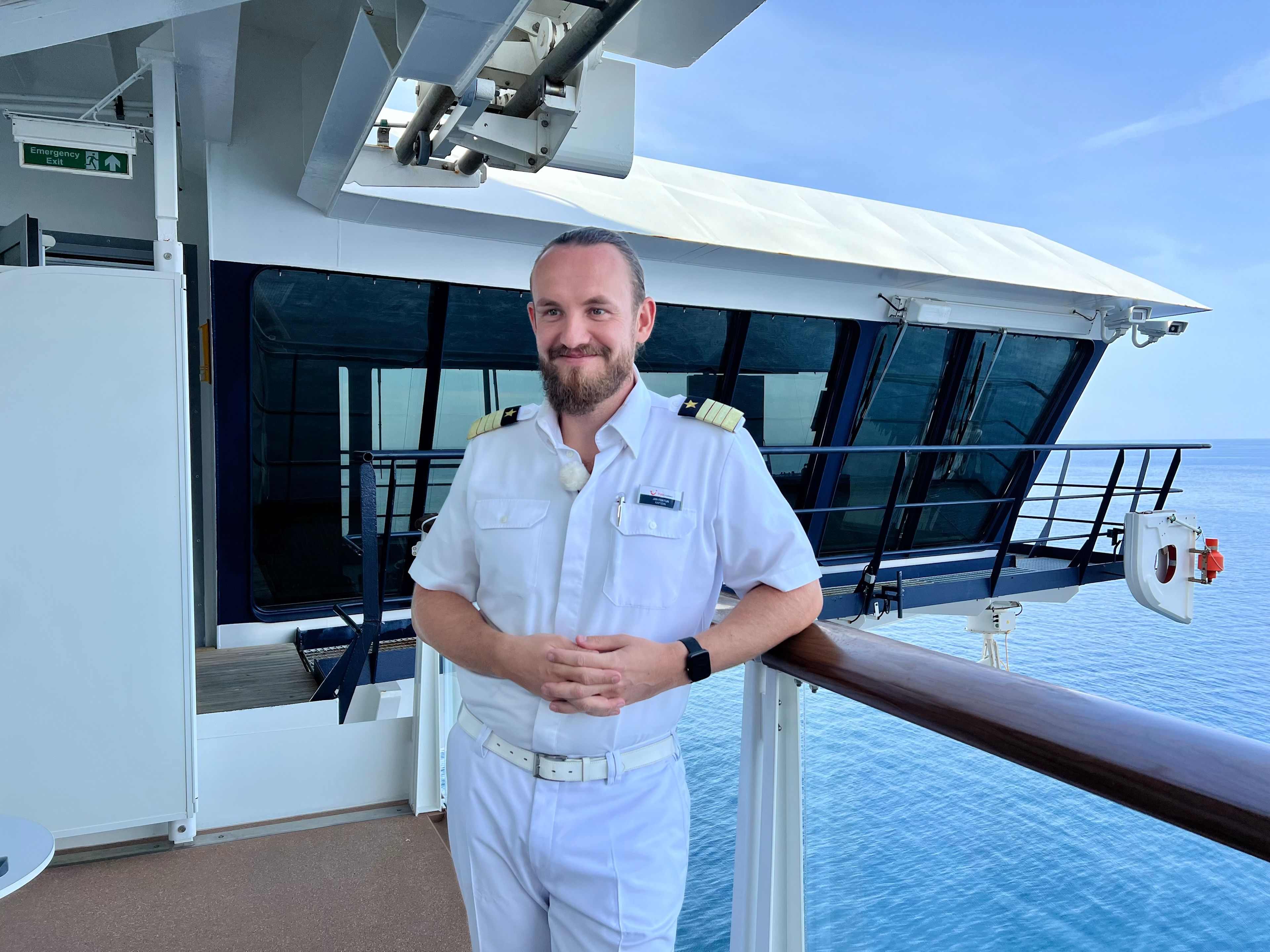 Mann in weißer Uniform auf Kreuzfahrtschiff der Mein Schiff® Flotte, Meer im Hintergrund.
