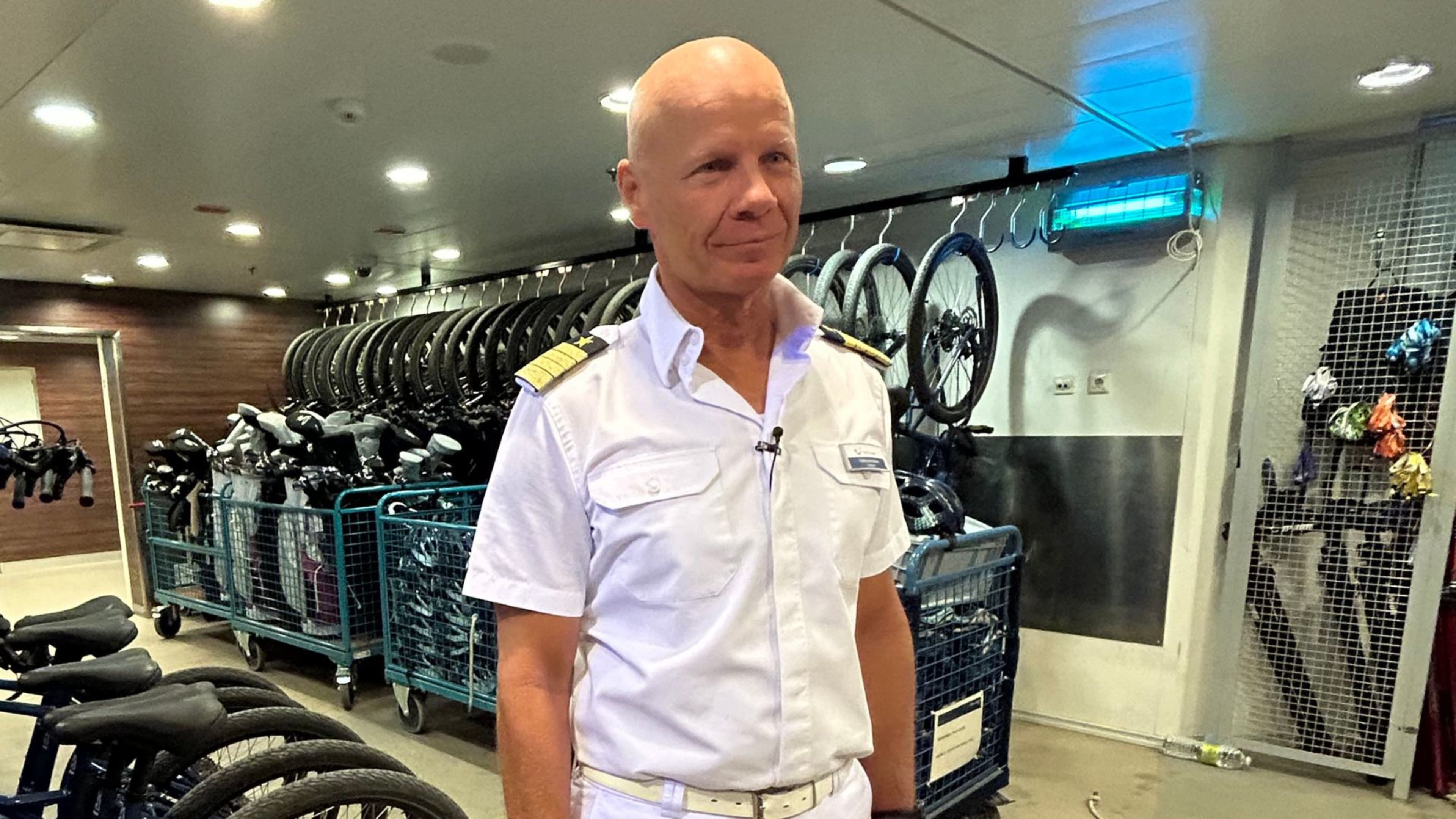 Mann in weißer Uniform vor Fahrrädern auf Kreuzfahrtschiff. Mann in weißer Uniform vor Fahrrädern auf Kreuzfahrtschiff.