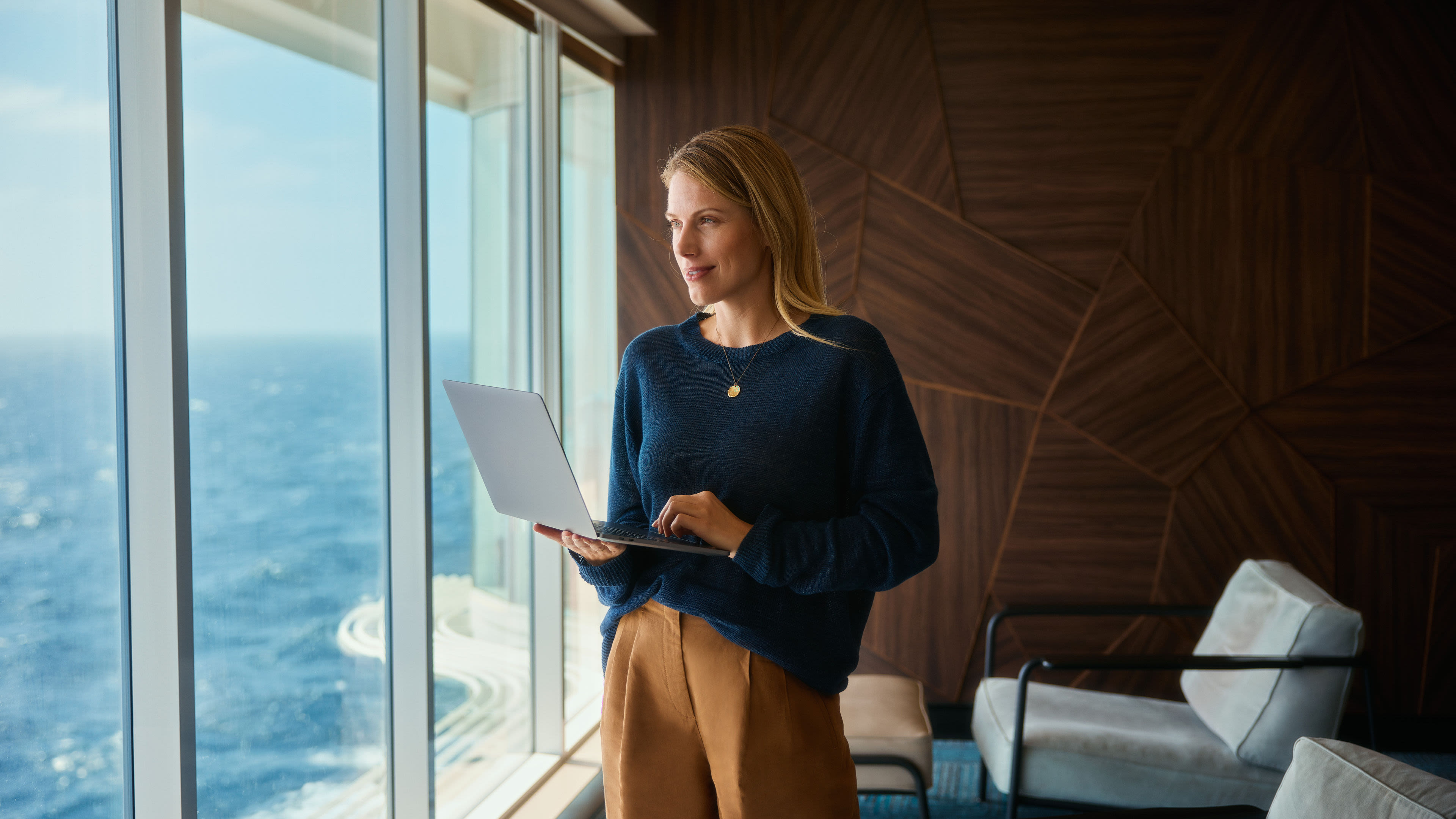 Frau mit Laptop, blickt aus Fenster auf Meer. Frau mit Laptop, blickt aus Fenster auf Meer.