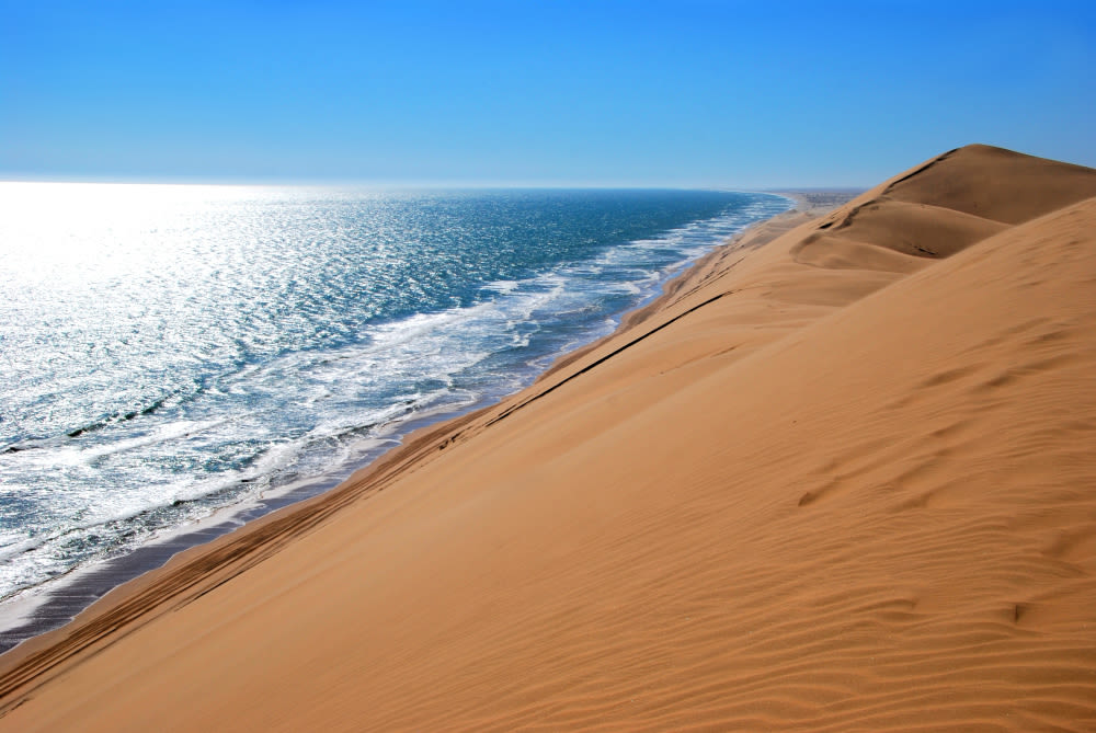 Sanddünen treffen auf das Meer unter blauem Himmel. Sanddünen treffen auf das Meer unter blauem Himmel.