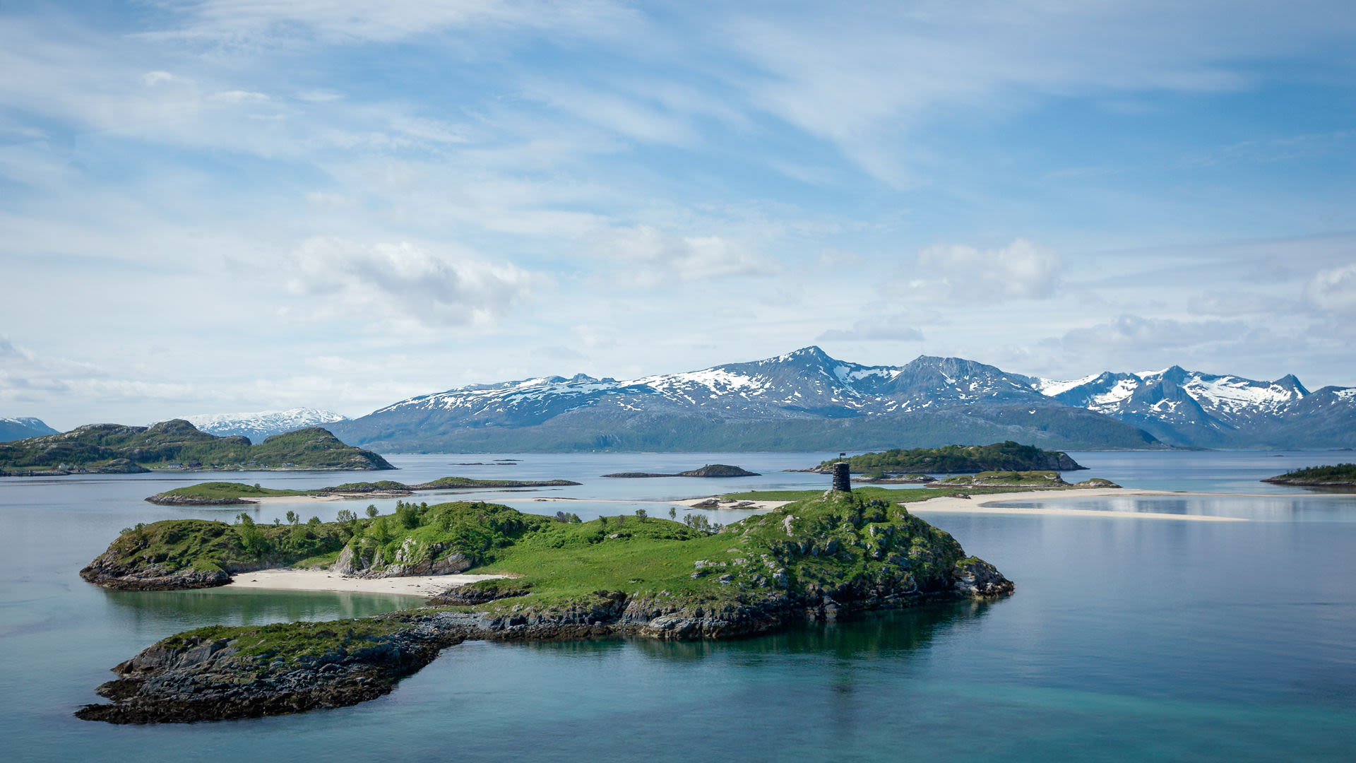 Grüne Inseln im blauen Fjord vor schneebedeckten Bergen in Norwegen.