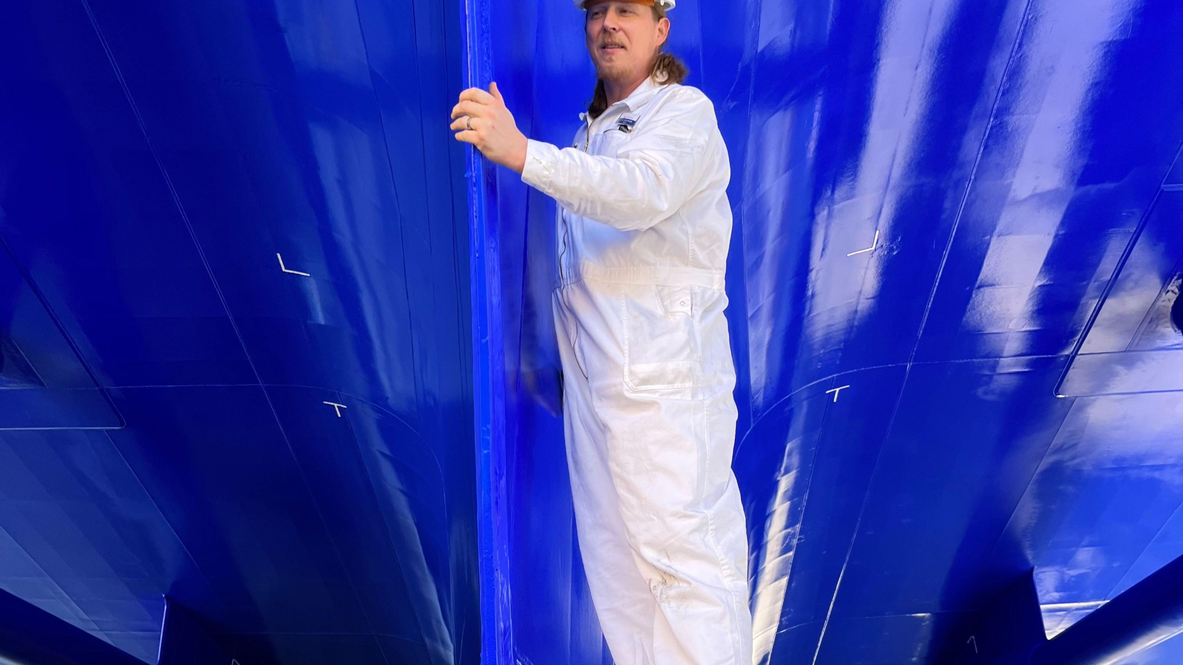 Mann in weißem Overall unter blauem Schiffsrumpf. Mann in weißem Overall unter blauem Schiffsrumpf.