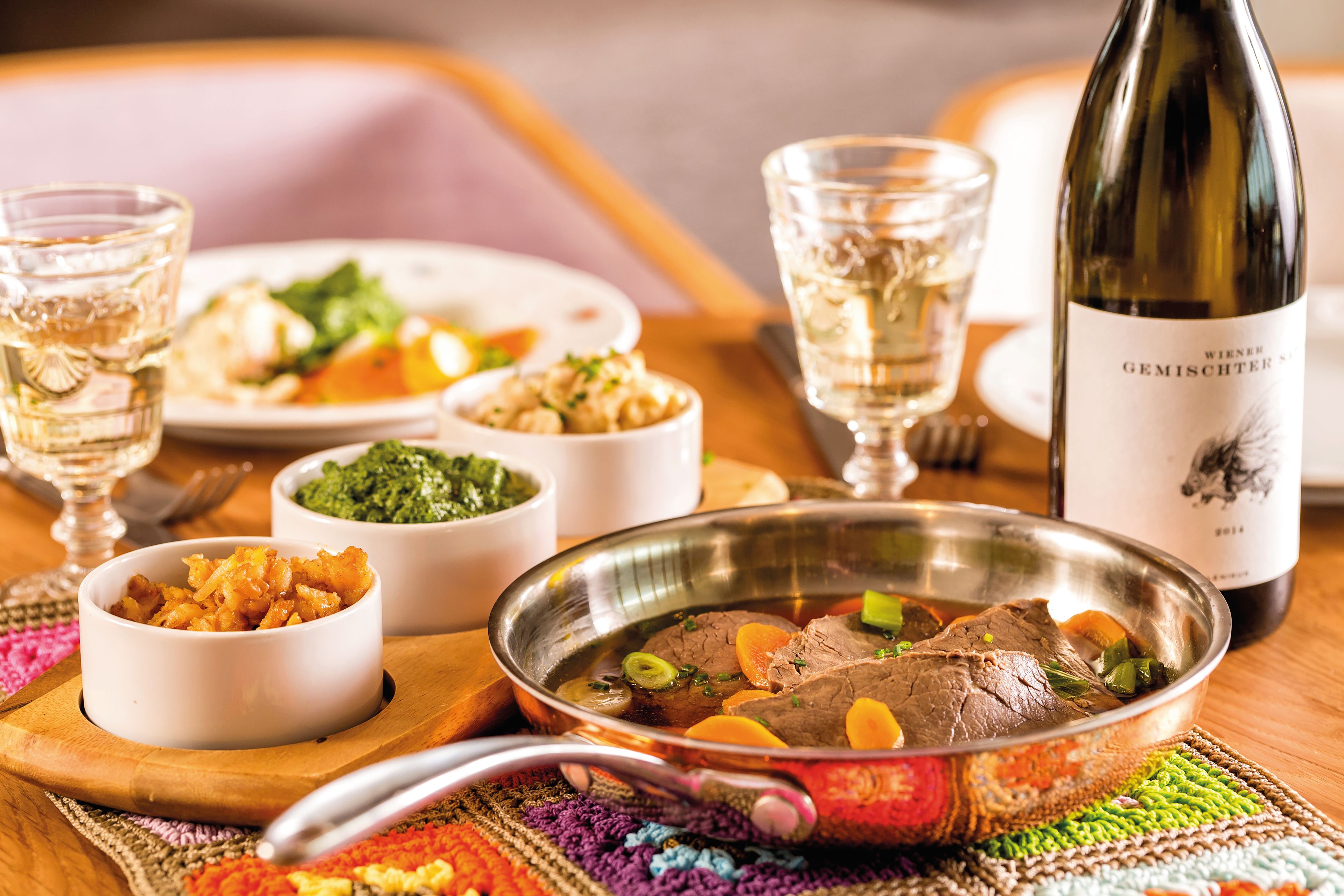 Tafelspitz mit Beilagen, Weißwein und Gemüse auf Holztisch.