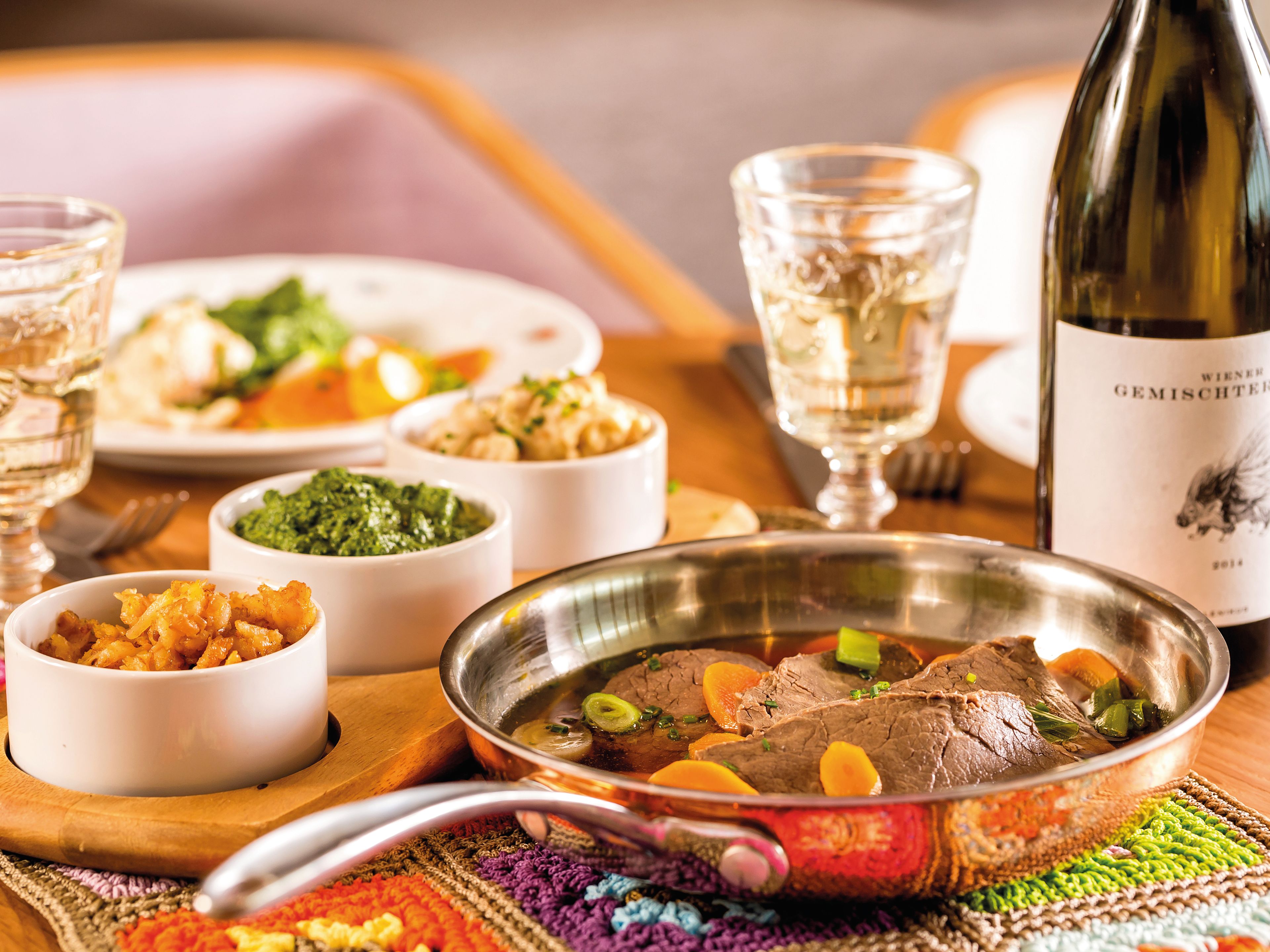 Tafelspitz mit Beilagen, Weißwein und Gemüse auf Holztisch. Tafelspitz mit Beilagen, Weißwein und Gemüse auf Holztisch.