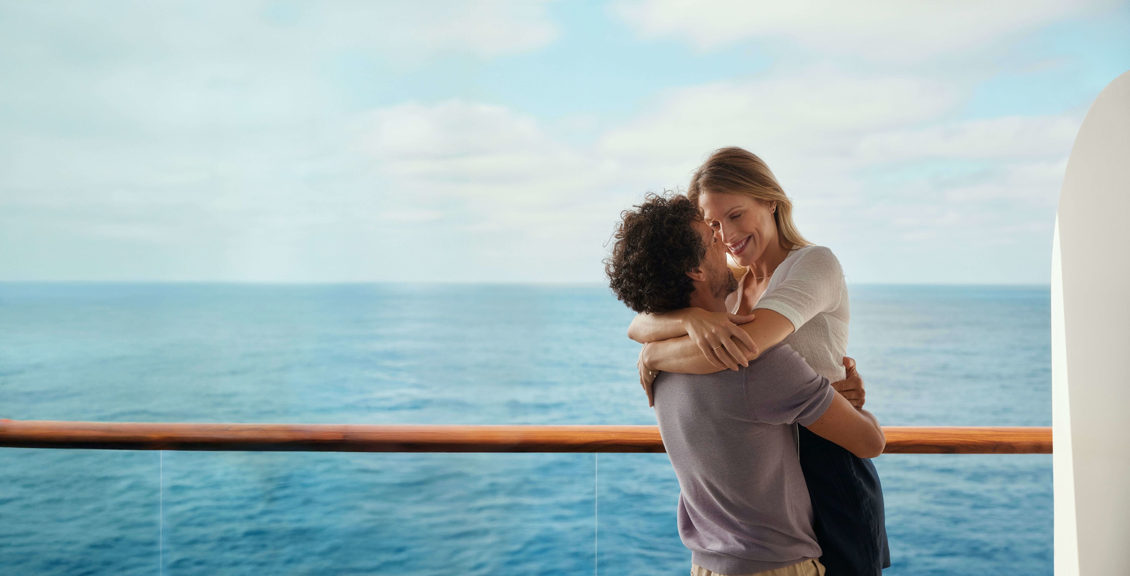Paar umarmt sich auf Kreuzfahrtschiff, Meer im Hintergrund.