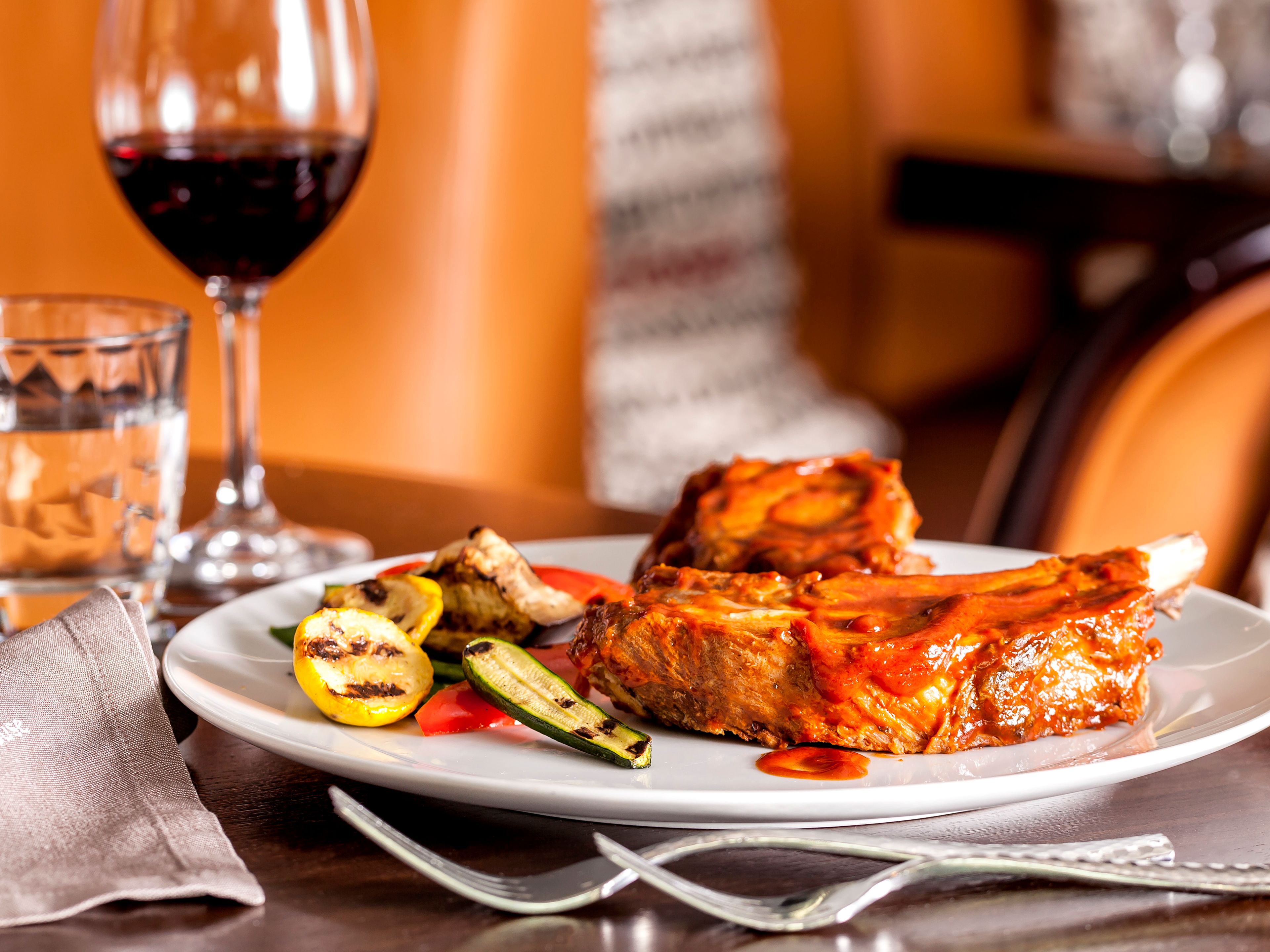 Rippchen mit gegrilltem Gemüse, Rotwein und Wasser auf Holztisch. Rippchen mit gegrilltem Gemüse, Rotwein und Wasser auf Holztisch.