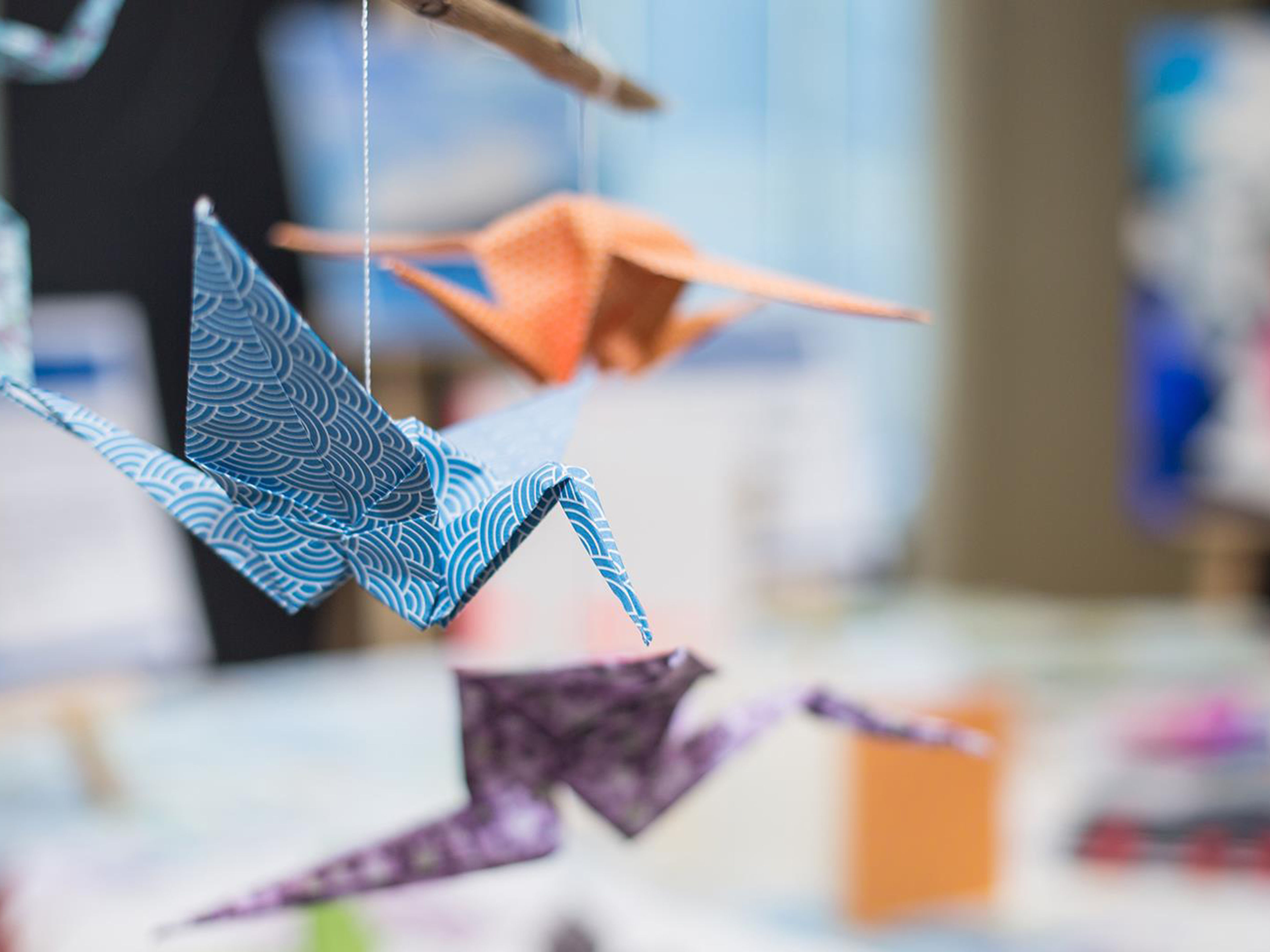 Bunte Origami-Kraniche hängen an Fäden, unscharfer Hintergrund. Bunte Origami-Kraniche hängen an Fäden, unscharfer Hintergrund.