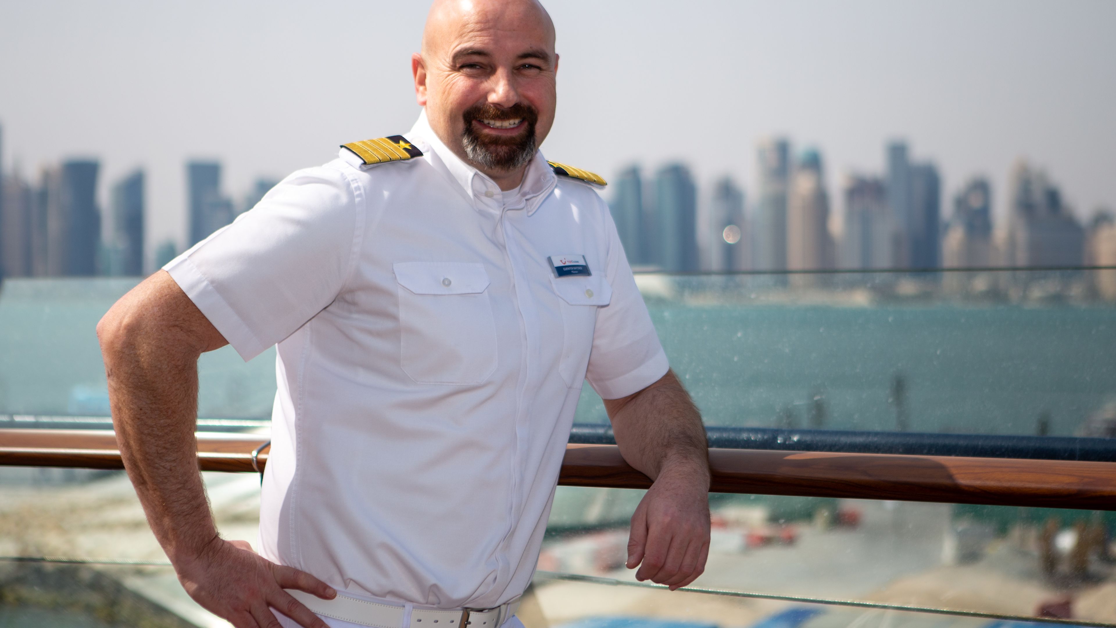 Mann in weißer Uniform auf Kreuzfahrtschiff, Skyline im Hintergrund. Mann in weißer Uniform auf Kreuzfahrtschiff, Skyline im Hintergrund.