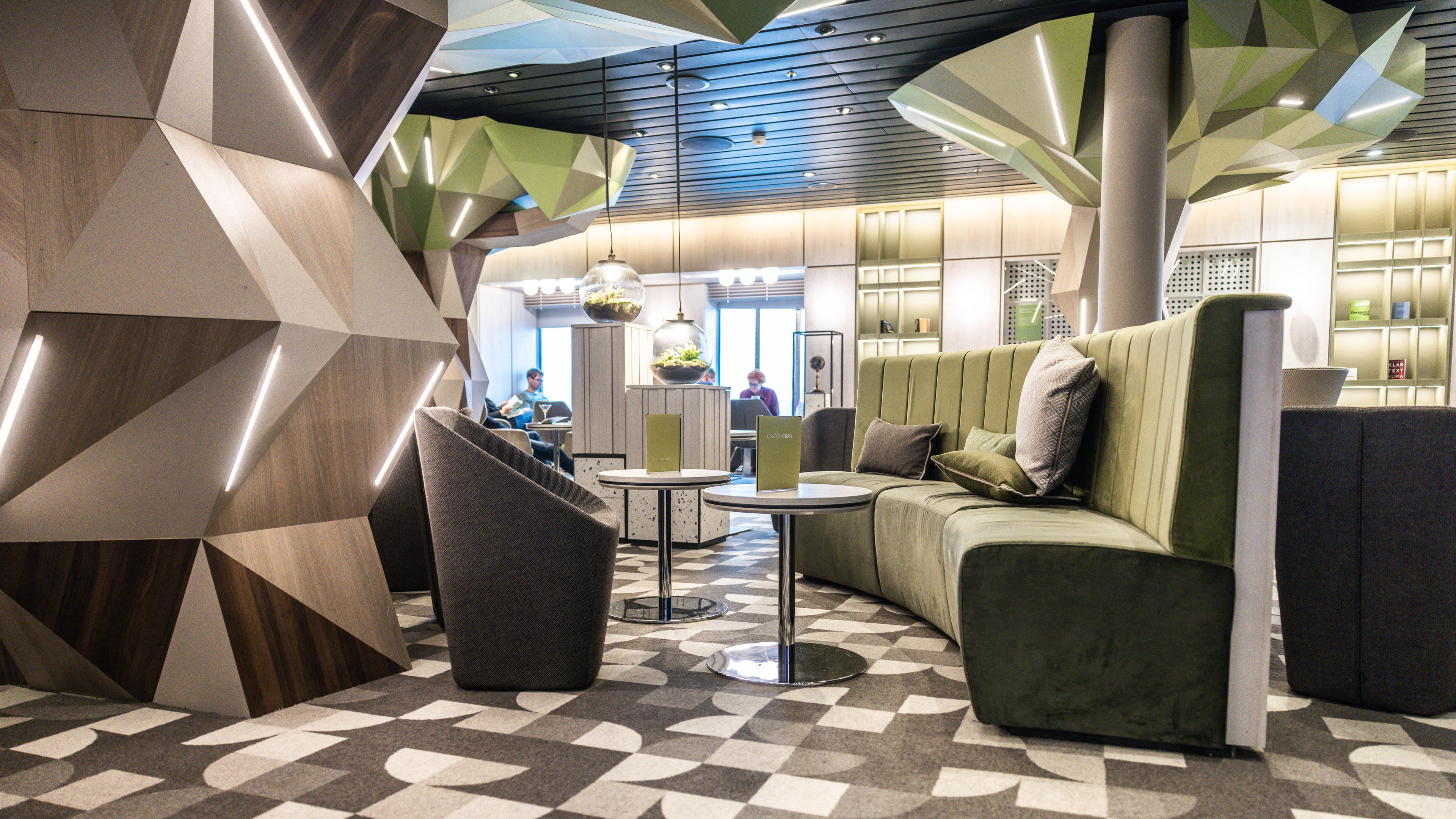Moderne Lounge mit grünen Sofas, geometrischen Wänden und hängenden Pflanzen.