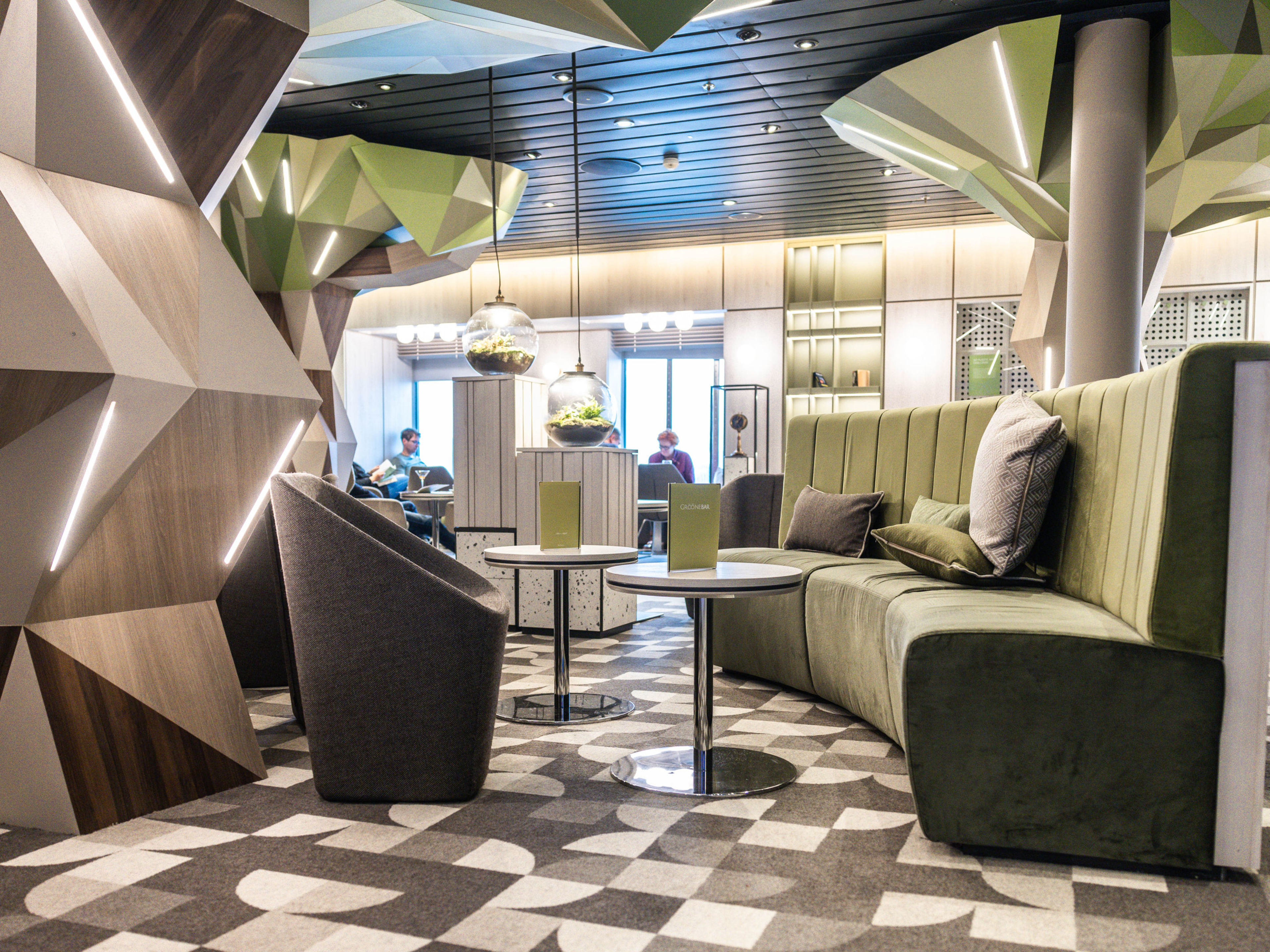 Moderne Lounge mit grünen Sofas, geometrischen Wänden und hängenden Pflanzen. Moderne Lounge mit grünen Sofas, geometrischen Wänden und hängenden Pflanzen.