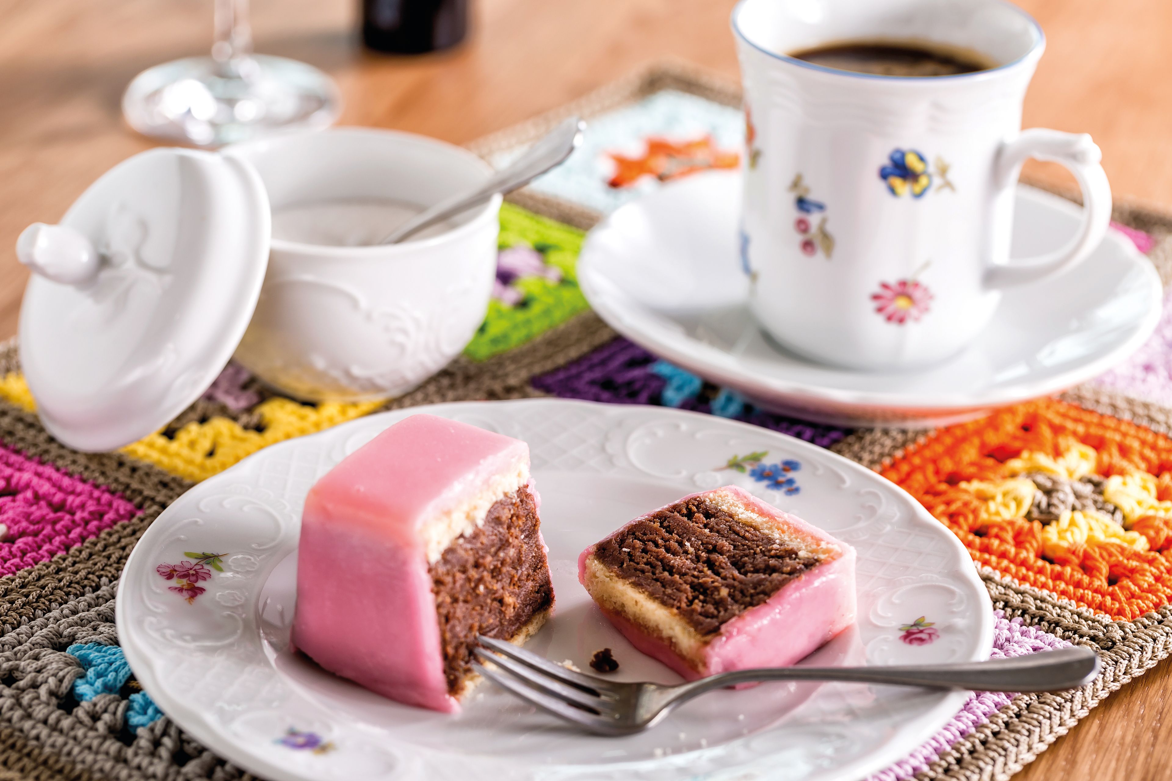 Teegebäck mit rosa Glasur und Kaffee auf bunter Tischdecke.