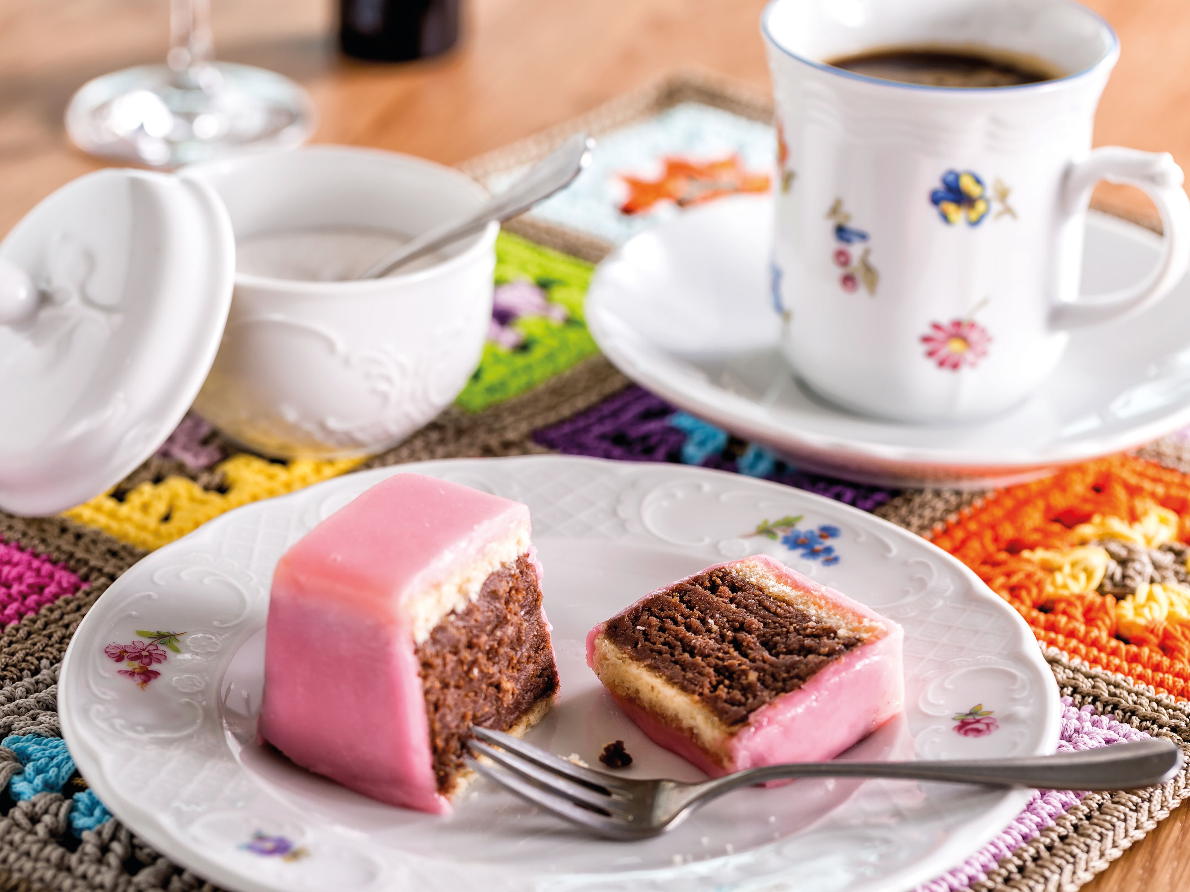 Teegebäck mit rosa Glasur und Kaffee auf bunter Tischdecke. Teegebäck mit rosa Glasur und Kaffee auf bunter Tischdecke.