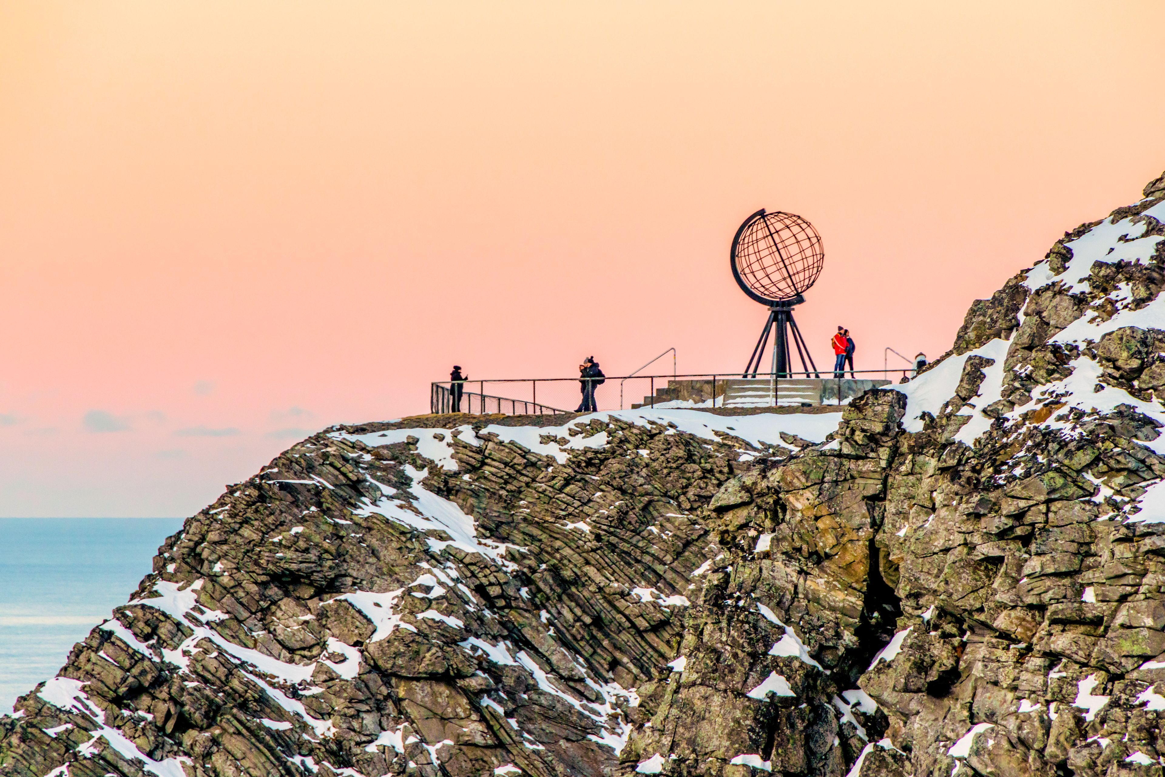 Nordkap-Globus bei Sonnenuntergang, schneebedeckte Klippen, Menschen auf Aussichtsplattform.