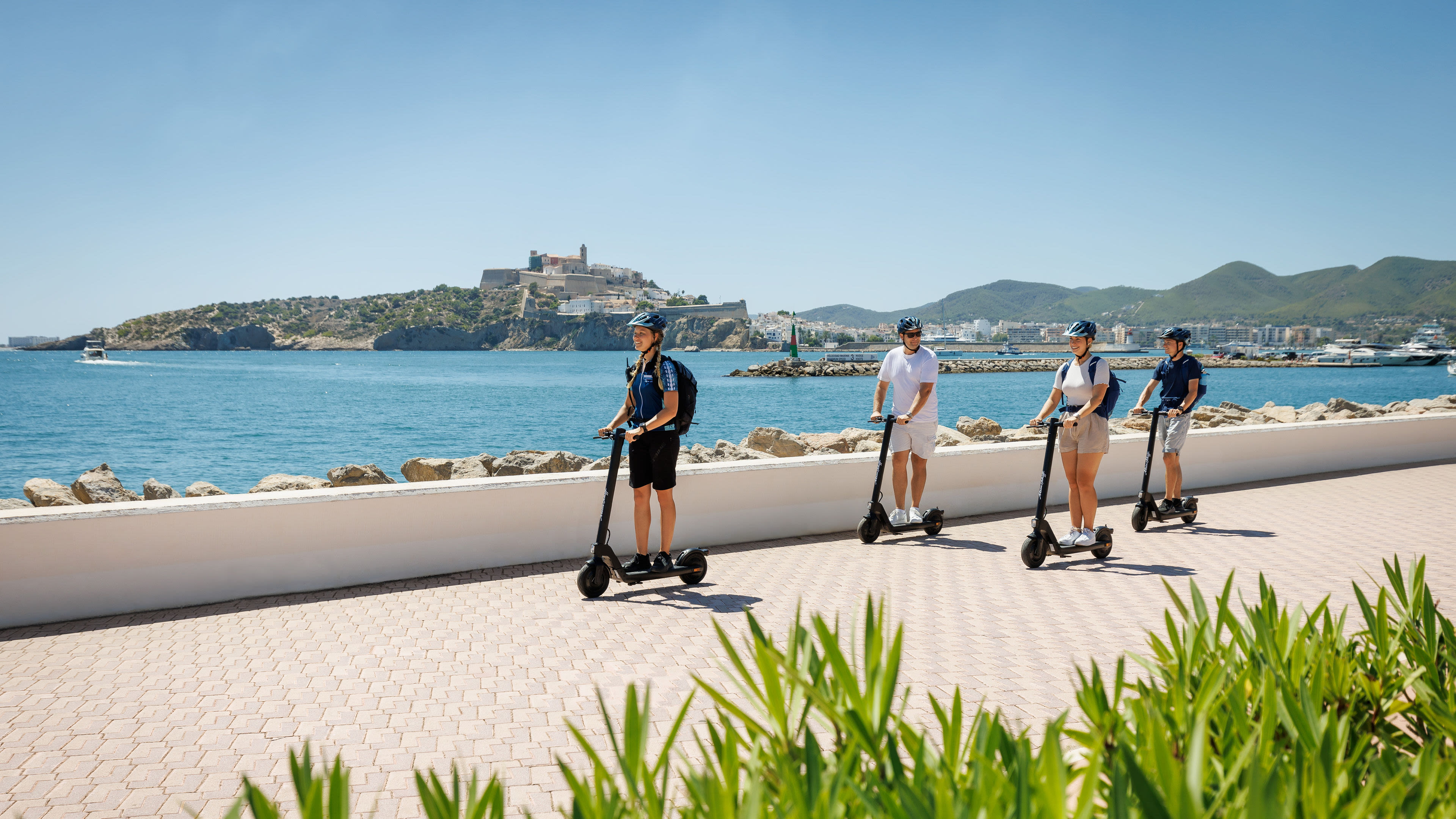 Vier Personen fahren E-Scooter entlang der Küste von Ibiza. Vier Personen fahren E-Scooter entlang der Küste von Ibiza.
