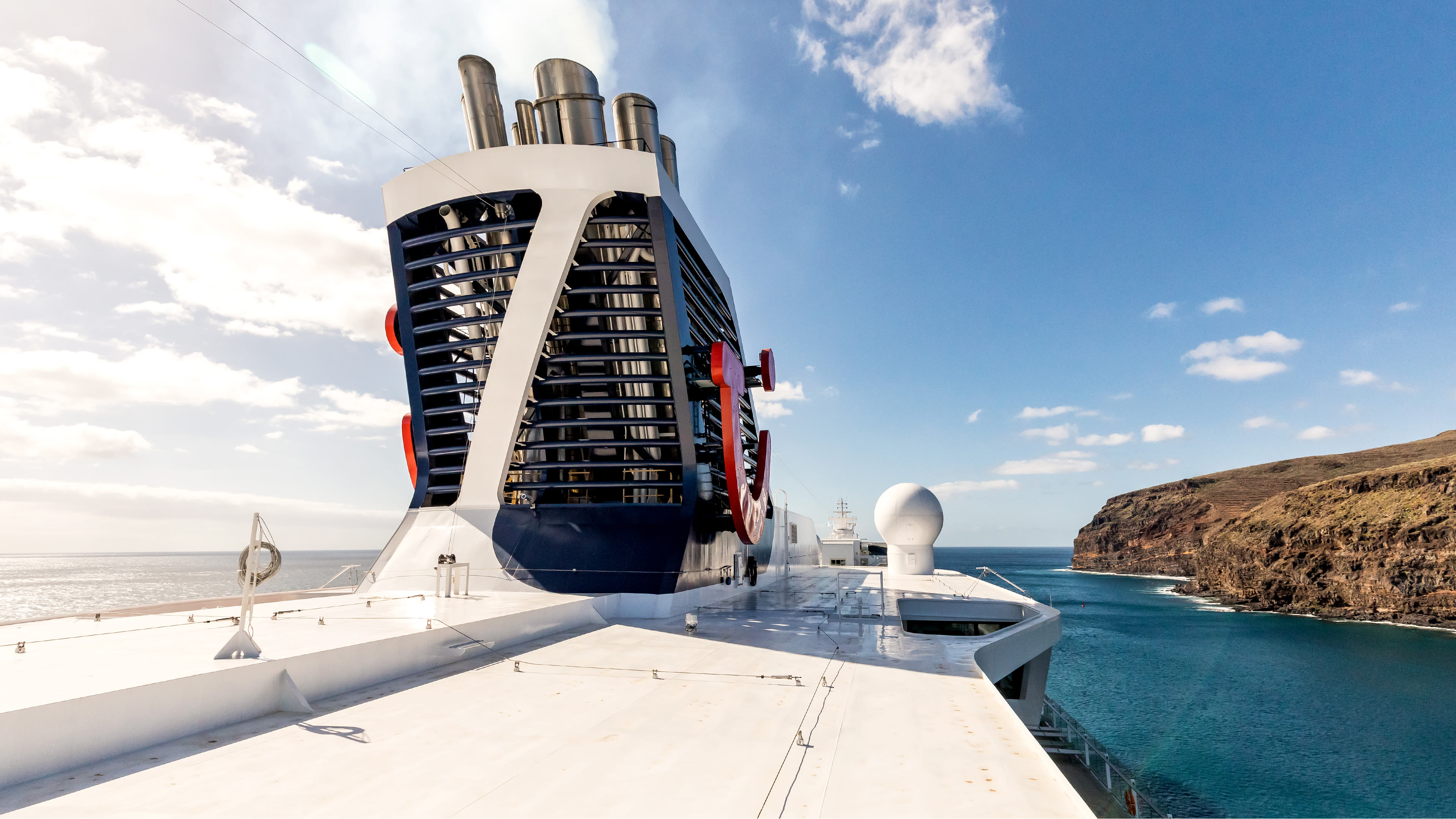 Kreuzfahrtschiff der Mein Schiff® Flotte vor felsiger Küste, blauer Himmel.