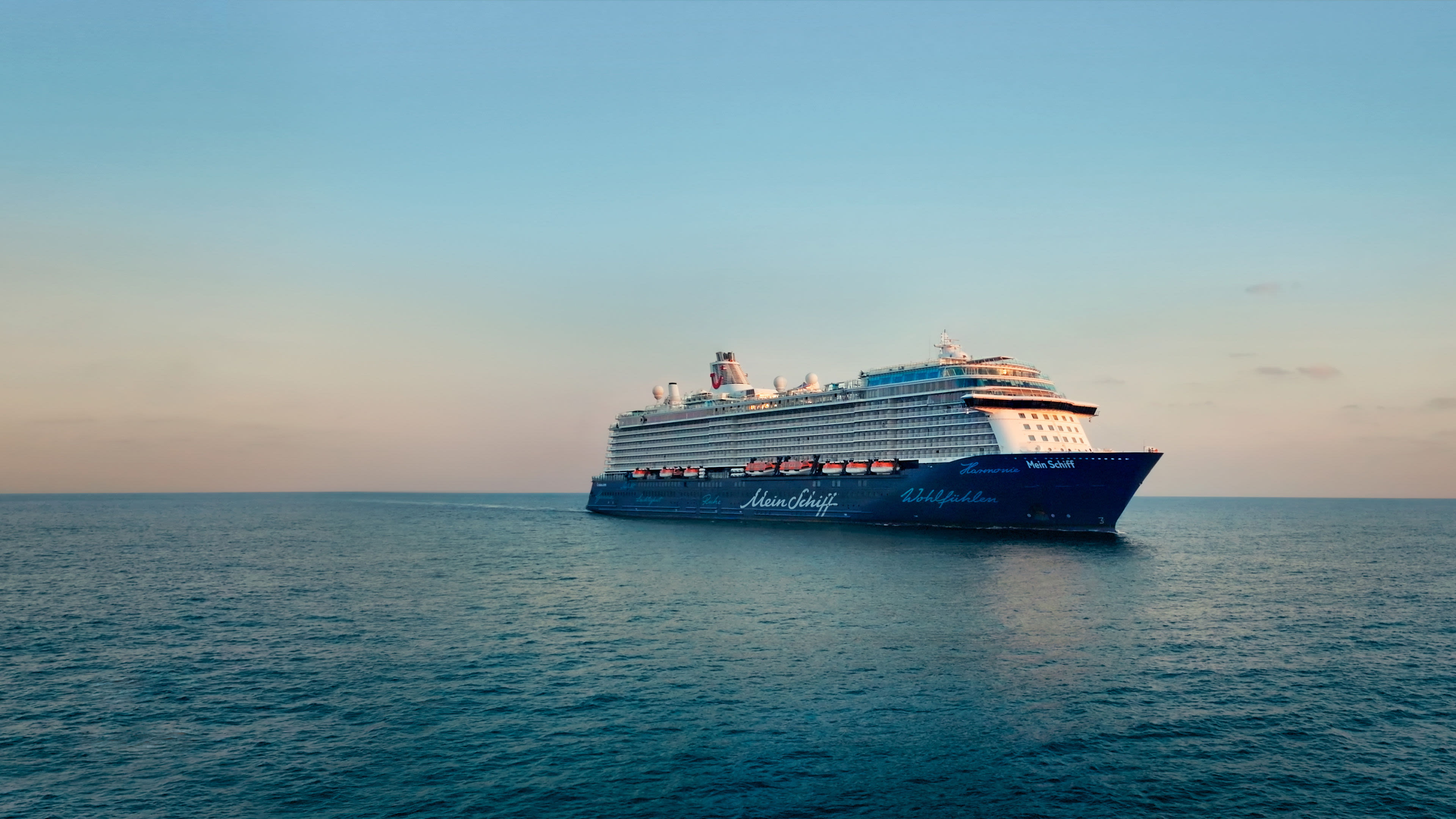 Kreuzfahrtschiff der Mein Schiff® Flotte auf offenem Meer bei Sonnenuntergang.