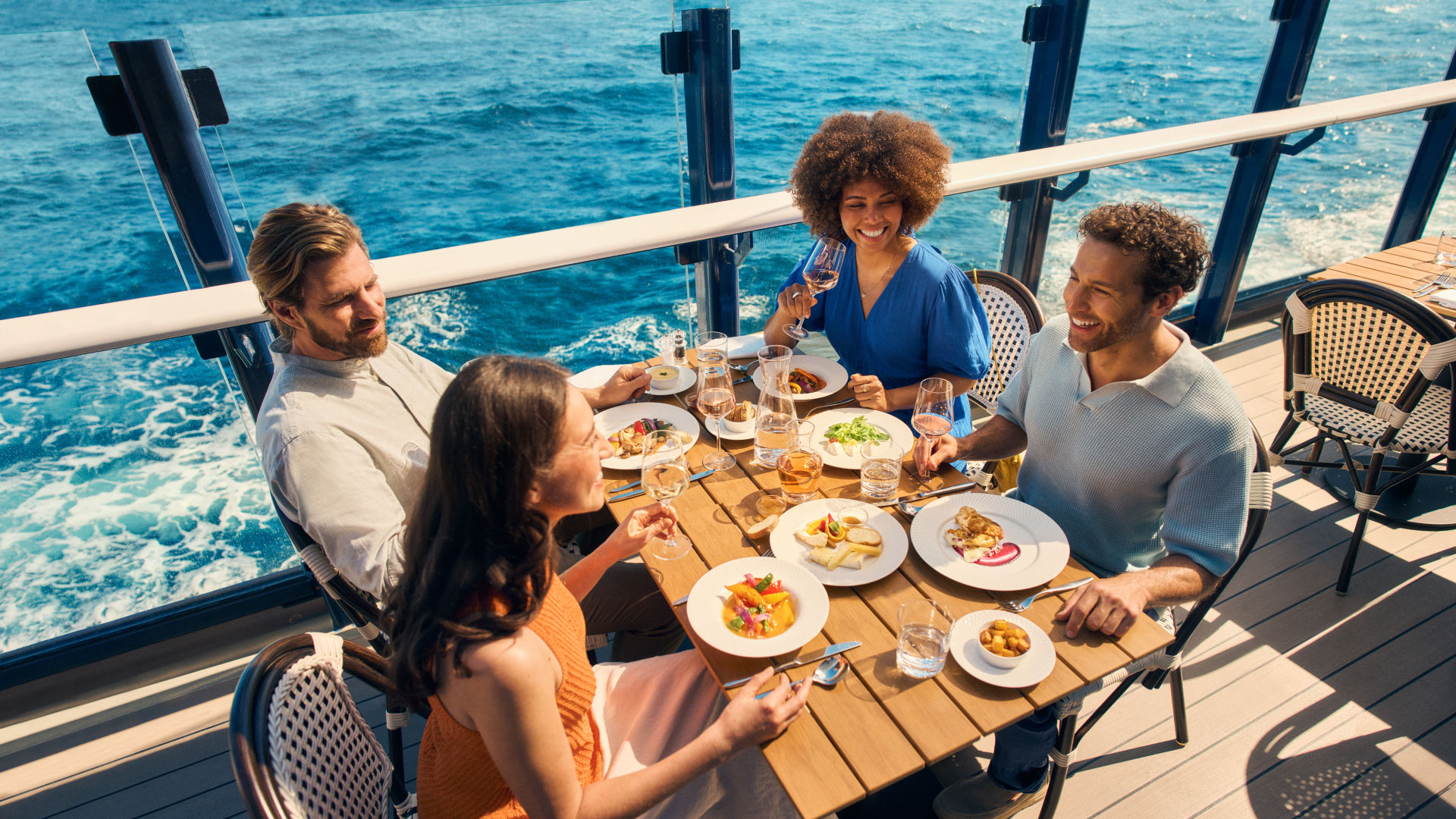 Vier Personen essen auf einem Kreuzfahrtschiff der Mein Schiff® Flotte mit Meerblick.