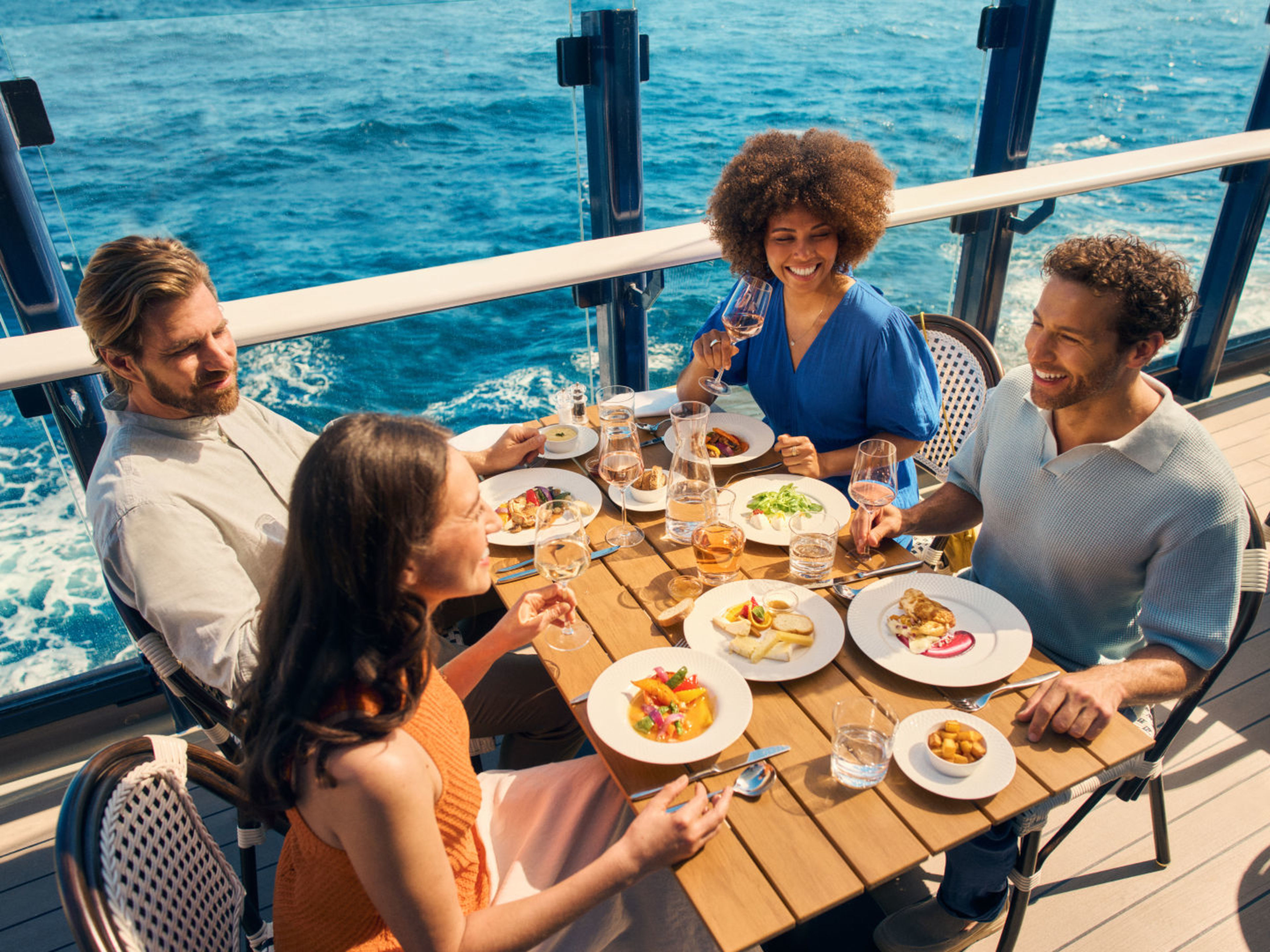Vier Personen essen auf einem Kreuzfahrtschiff der Mein Schiff® Flotte mit Meerblick. Vier Personen essen auf einem Kreuzfahrtschiff der Mein Schiff® Flotte mit Meerblick.