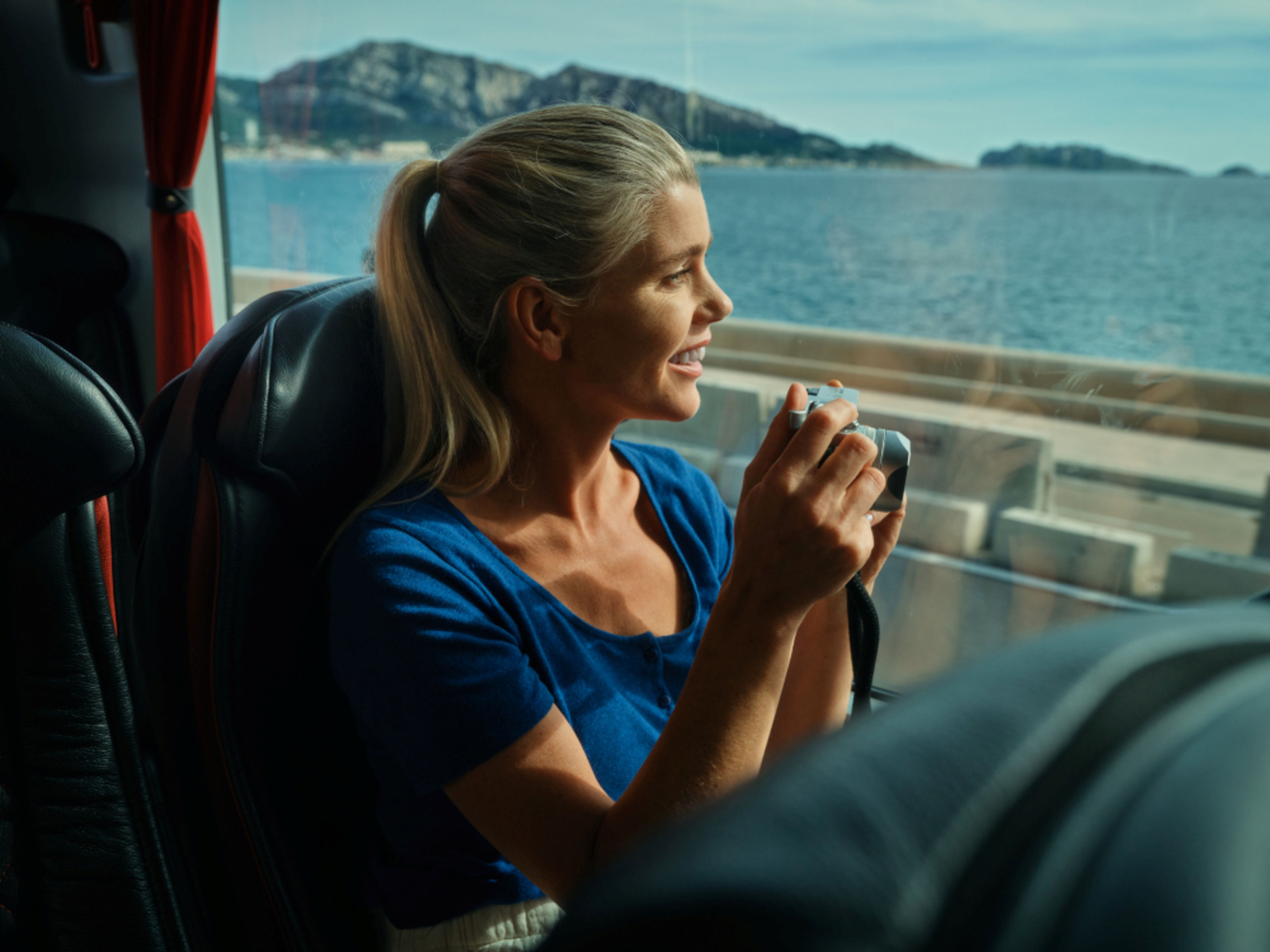 Frau im Bus mit Kamera, Meerblick, sonniger Tag. Frau im Bus mit Kamera, Meerblick, sonniger Tag.
