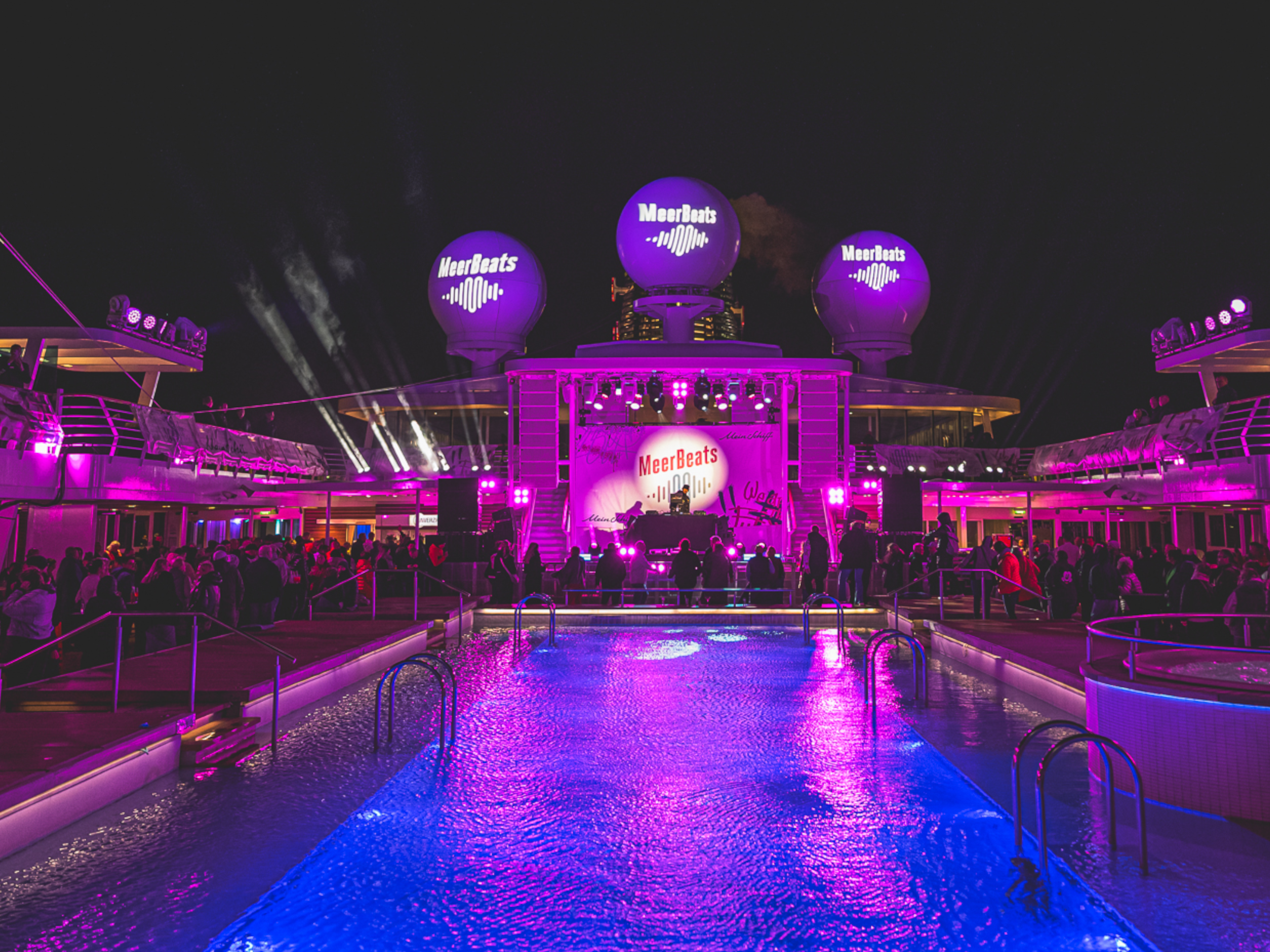 Nachtparty auf Kreuzfahrtschiff der Mein Schiff® Flotte, lila Beleuchtung, Pool, Menschenmenge. Nachtparty auf Kreuzfahrtschiff der Mein Schiff® Flotte, lila Beleuchtung, Pool, Menschenmenge.