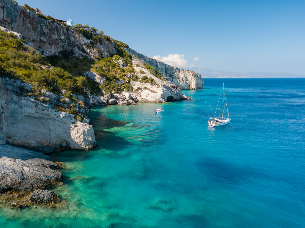 Segelboot im türkisblauen Wasser vor felsiger Küste, sonniger Himmel. Segelboot im türkisblauen Wasser vor felsiger Küste, sonniger Himmel.