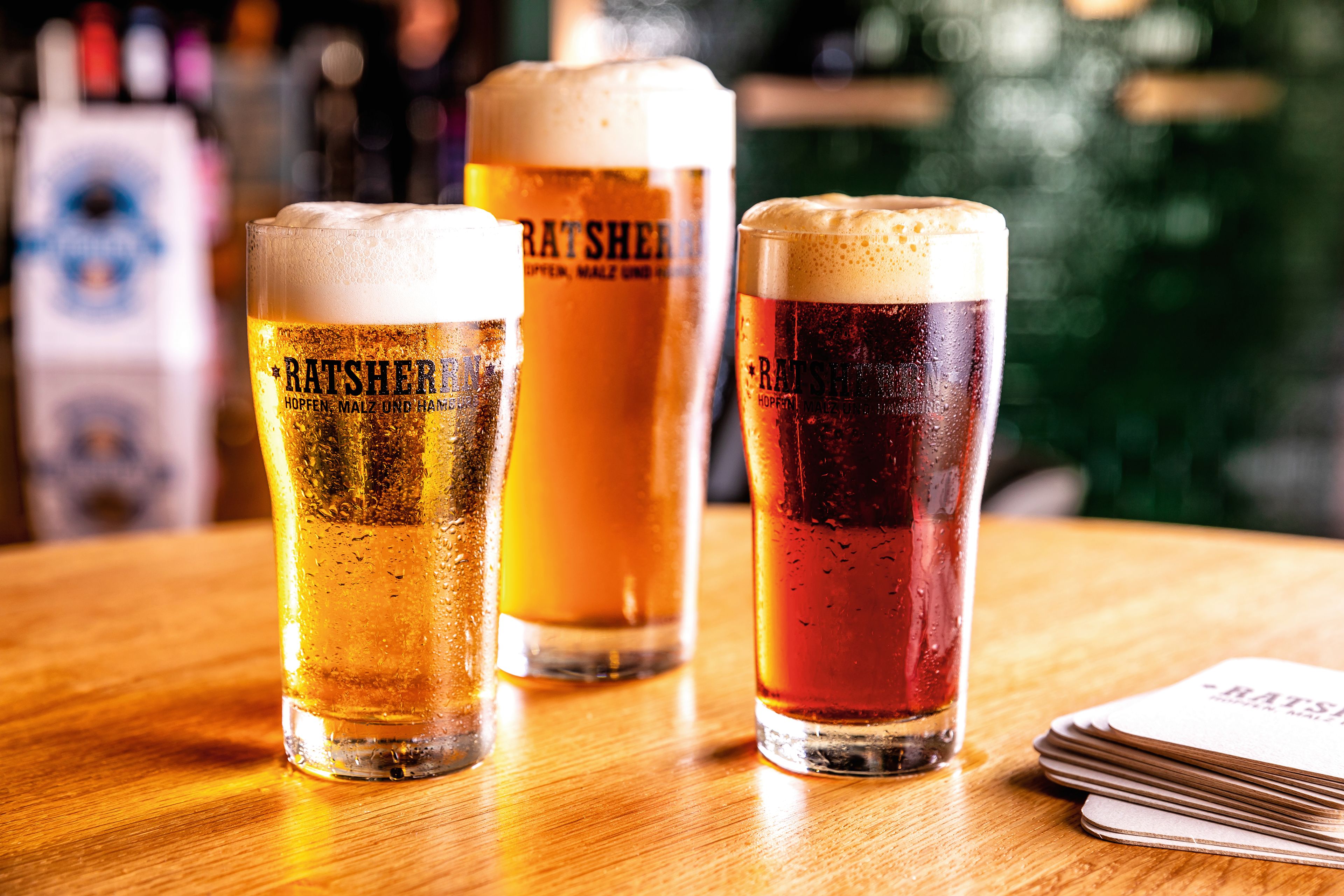 Drei Biergläser auf Holztisch, verschiedene Biersorten, Schaumkronen.