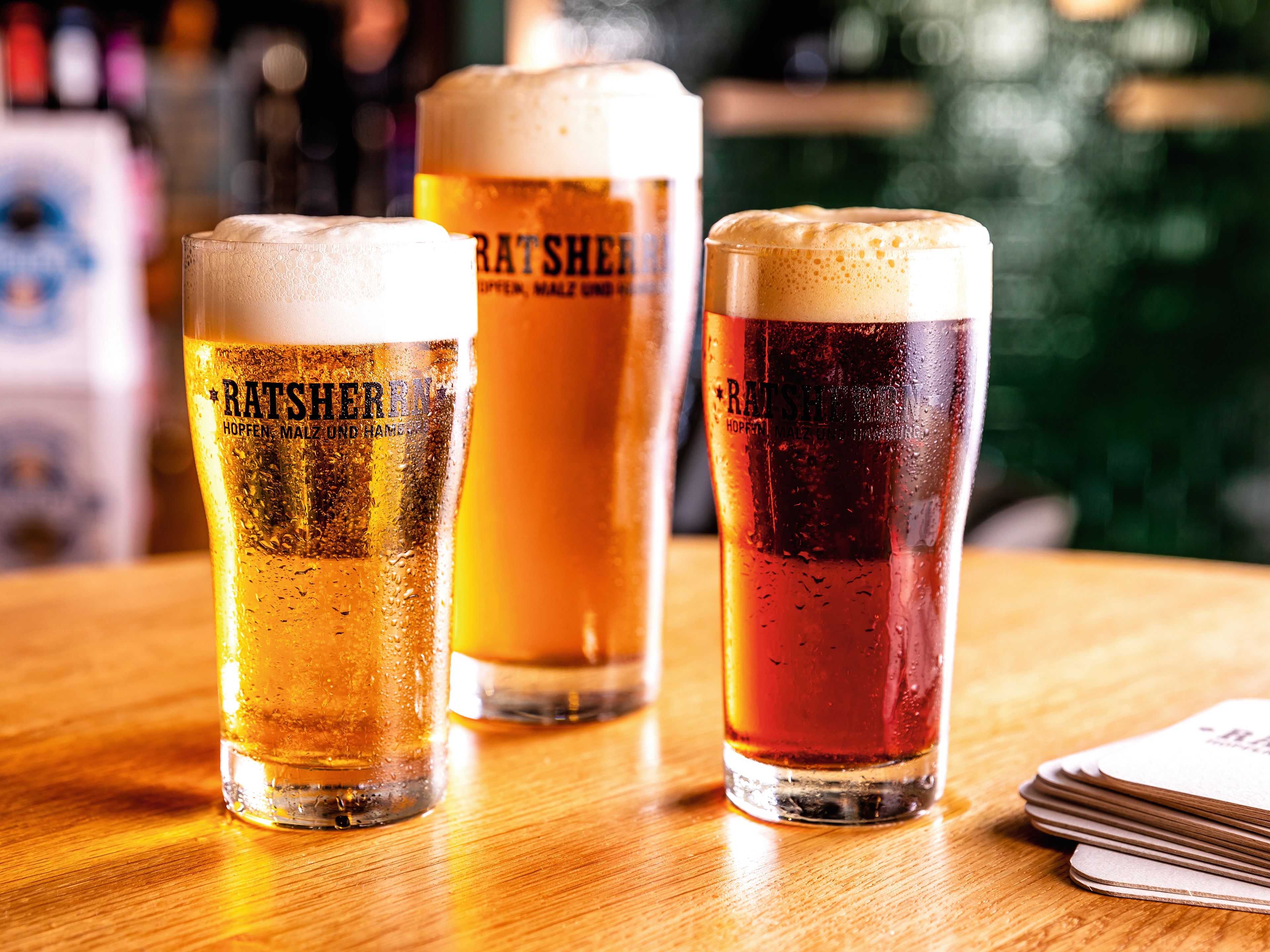 Drei Biergläser auf Holztisch, verschiedene Biersorten, Schaumkronen. Drei Biergläser auf Holztisch, verschiedene Biersorten, Schaumkronen.