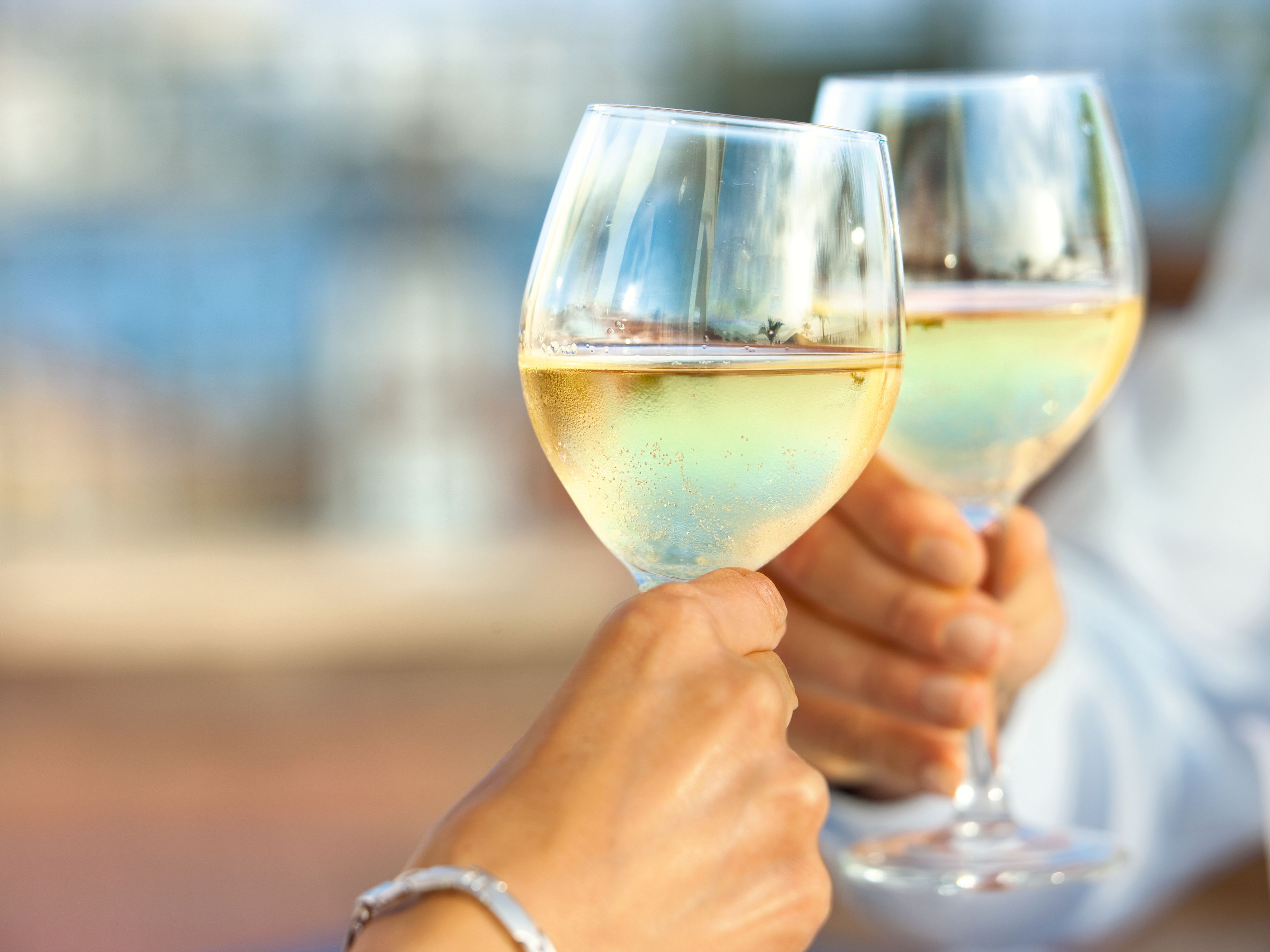 Zwei Personen stoßen mit Gläsern Weißwein an. Zwei Personen stoßen mit Gläsern Weißwein an.
