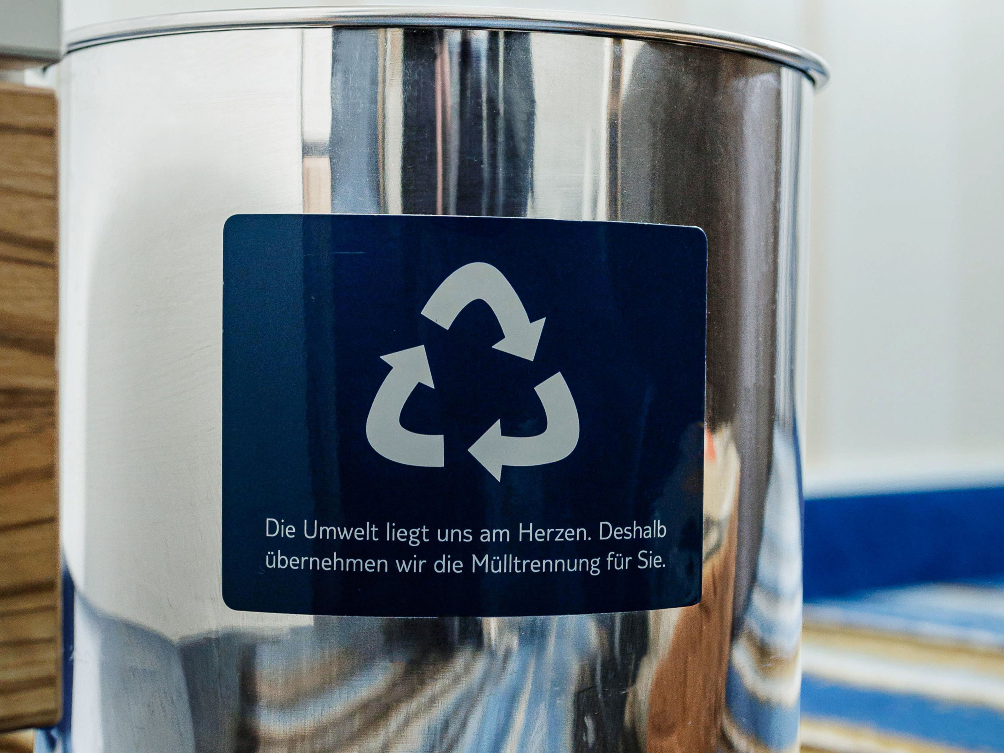 Recycling-Symbol auf silbernem Mülleimer mit Holz- und Teppichhintergrund. Recycling-Symbol auf silbernem Mülleimer mit Holz- und Teppichhintergrund.