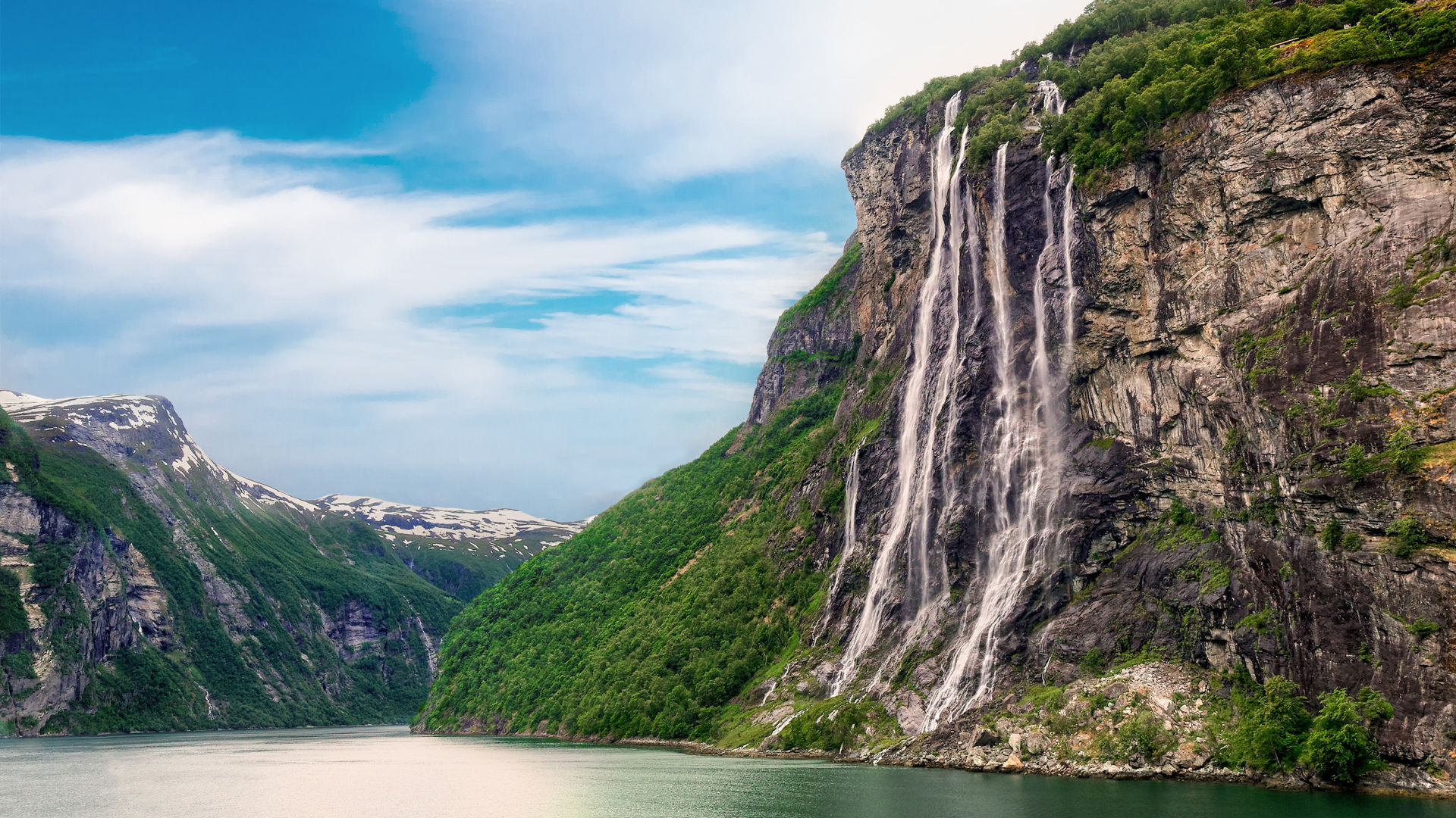 Wasserfall im Geirangerfjord, Norwegen, mit grünen Bergen und blauem Himmel.
