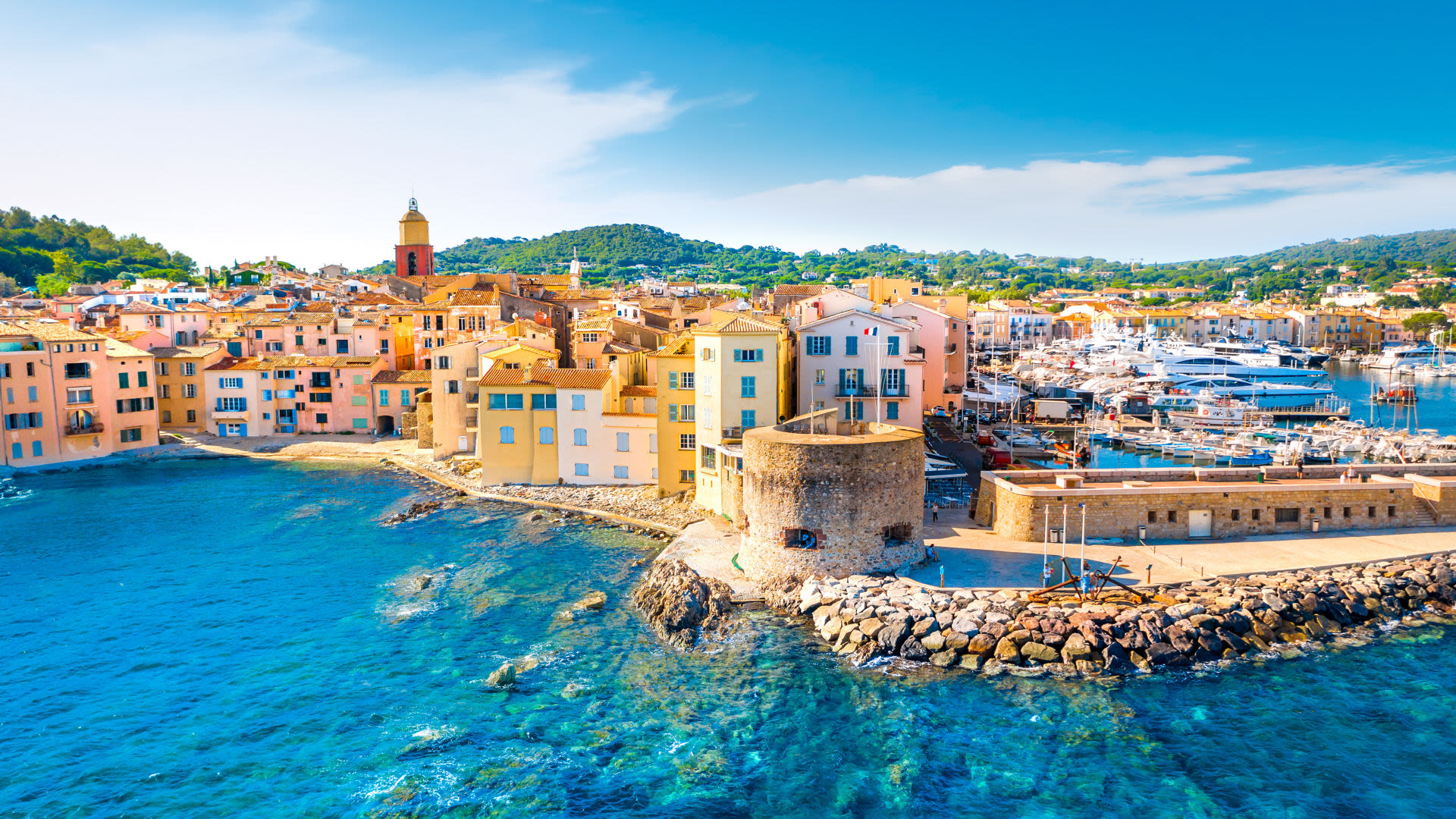Bunte Häuser und Hafen in Saint-Tropez, blaues Meer, sonniger Himmel.