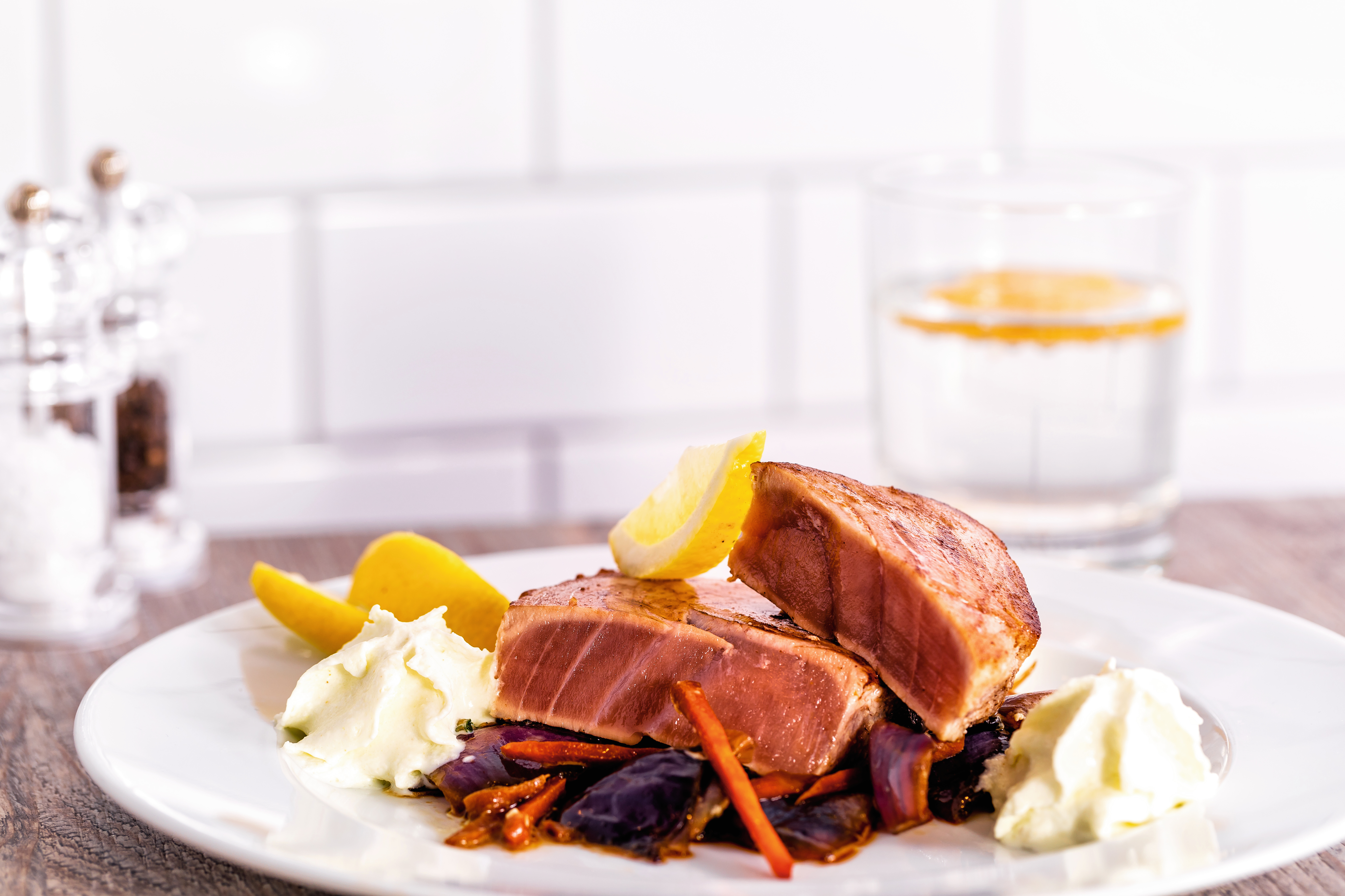 Gegrillter Thunfisch mit Zitronenscheiben, Gemüse und Kartoffelpüree auf weißem Teller.