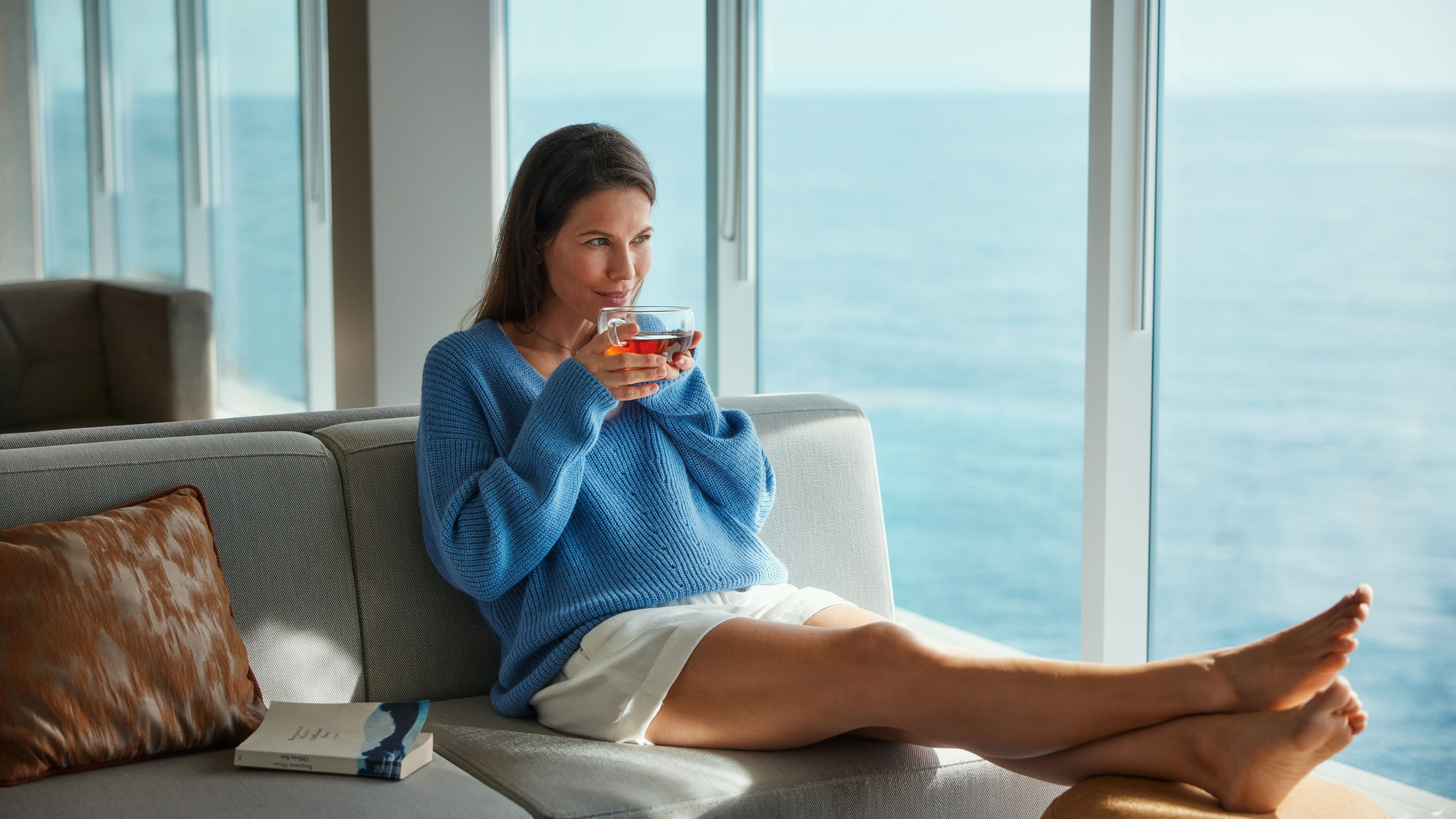 Frau in blauem Pullover trinkt Tee, Meerblick.