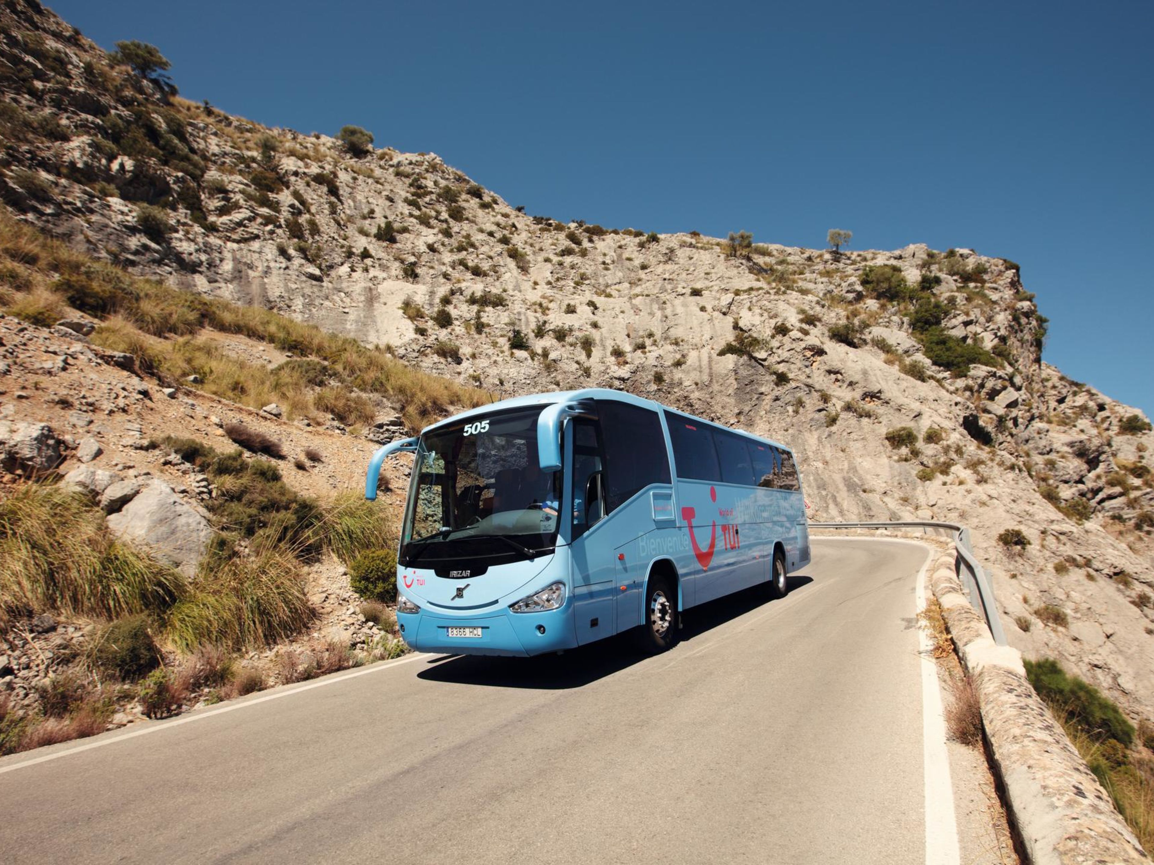 Blauer Reisebus auf kurviger Bergstraße bei Sonnenschein. Blauer Reisebus auf kurviger Bergstraße bei Sonnenschein.