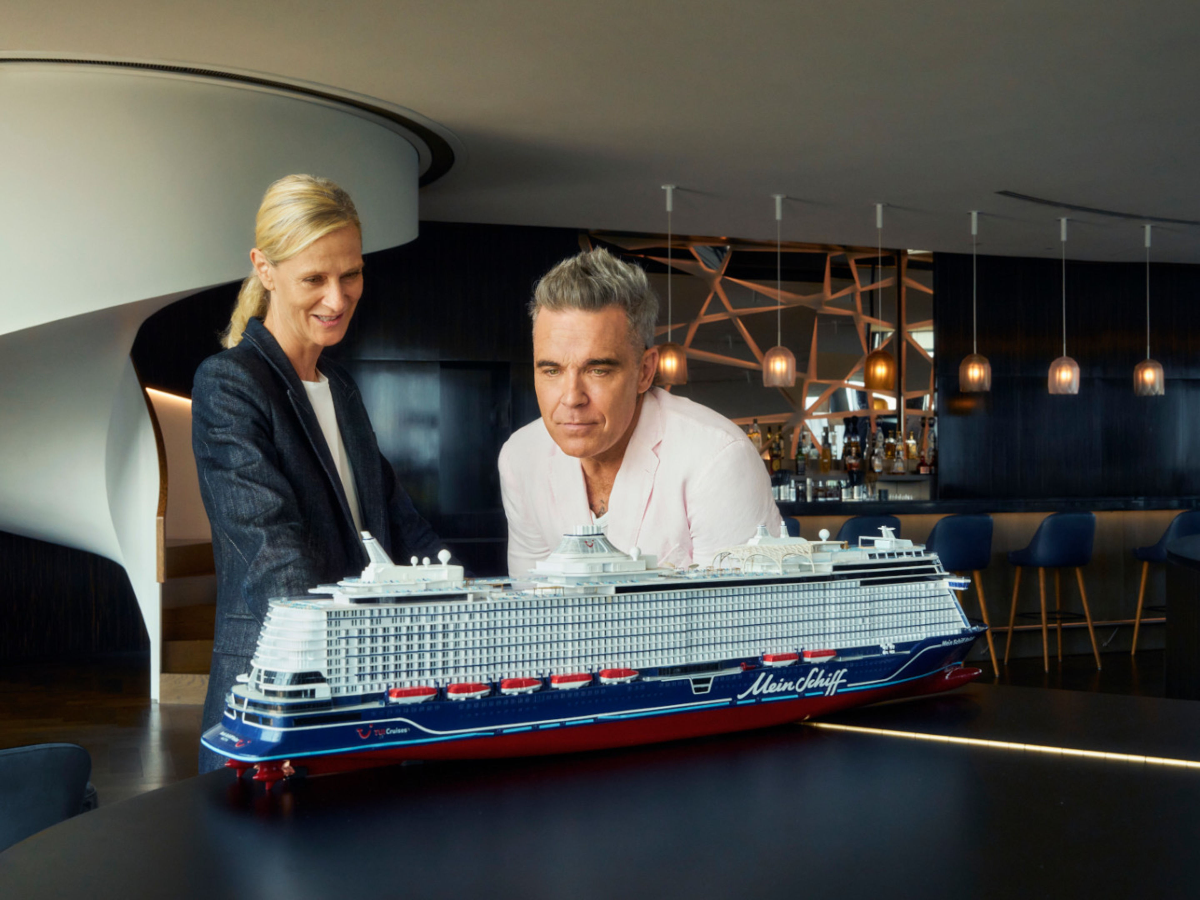 Zwei Personen betrachten Modell eines Kreuzfahrtschiffs der Mein Schiff® Flotte in modernem Raum. Zwei Personen betrachten Modell eines Kreuzfahrtschiffs der Mein Schiff® Flotte in modernem Raum.