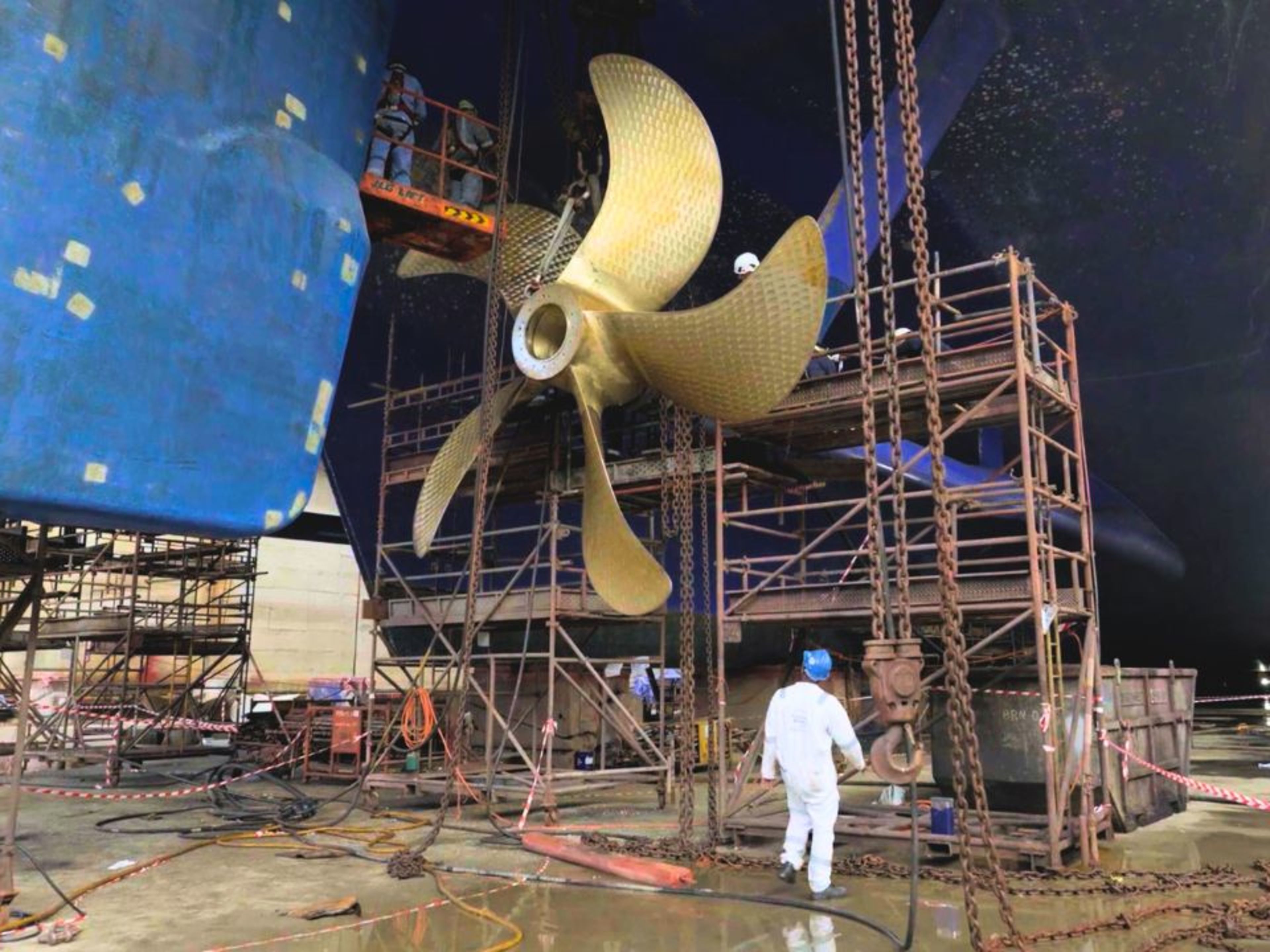 Arbeiter im Trockendock reparieren Schiffsschraube, Gerüste, blaue Schiffswand. Arbeiter im Trockendock reparieren Schiffsschraube, Gerüste, blaue Schiffswand.