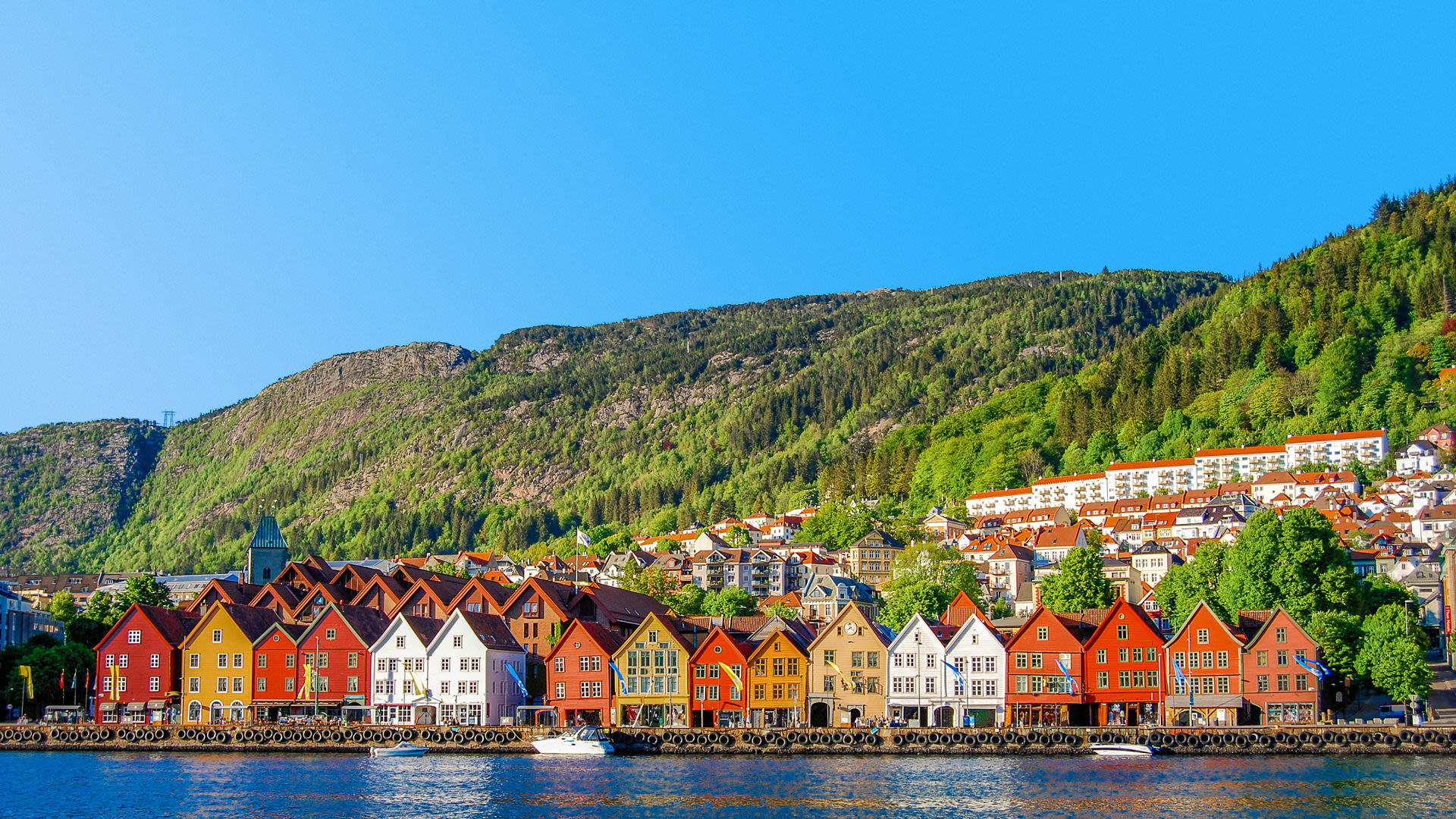Bunte Holzhäuser am Wasser in Bergen, Norwegen, vor grünen Hügeln.