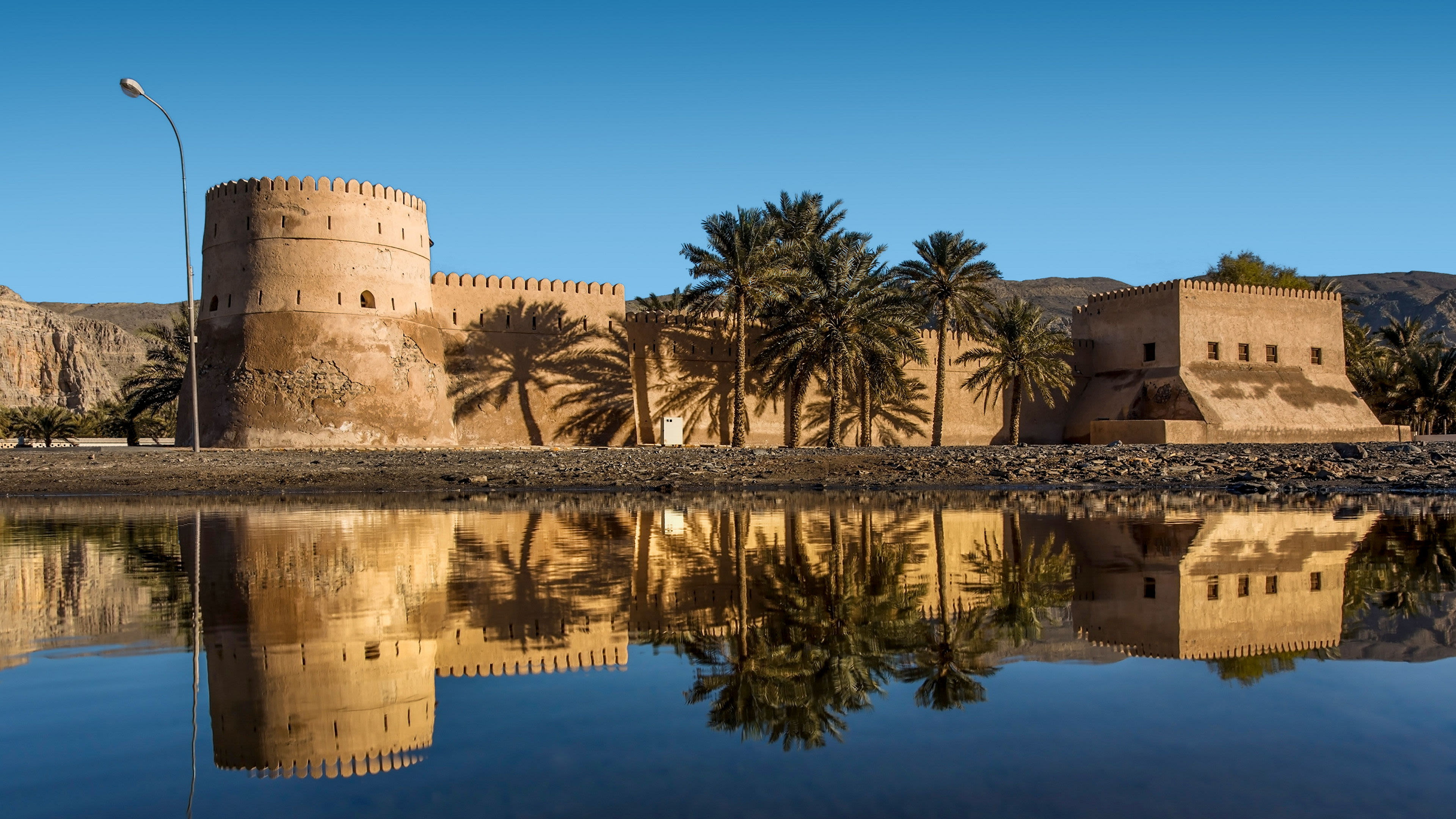 Altes Fort mit Palmen und Spiegelung im Wasser, blauer Himmel.