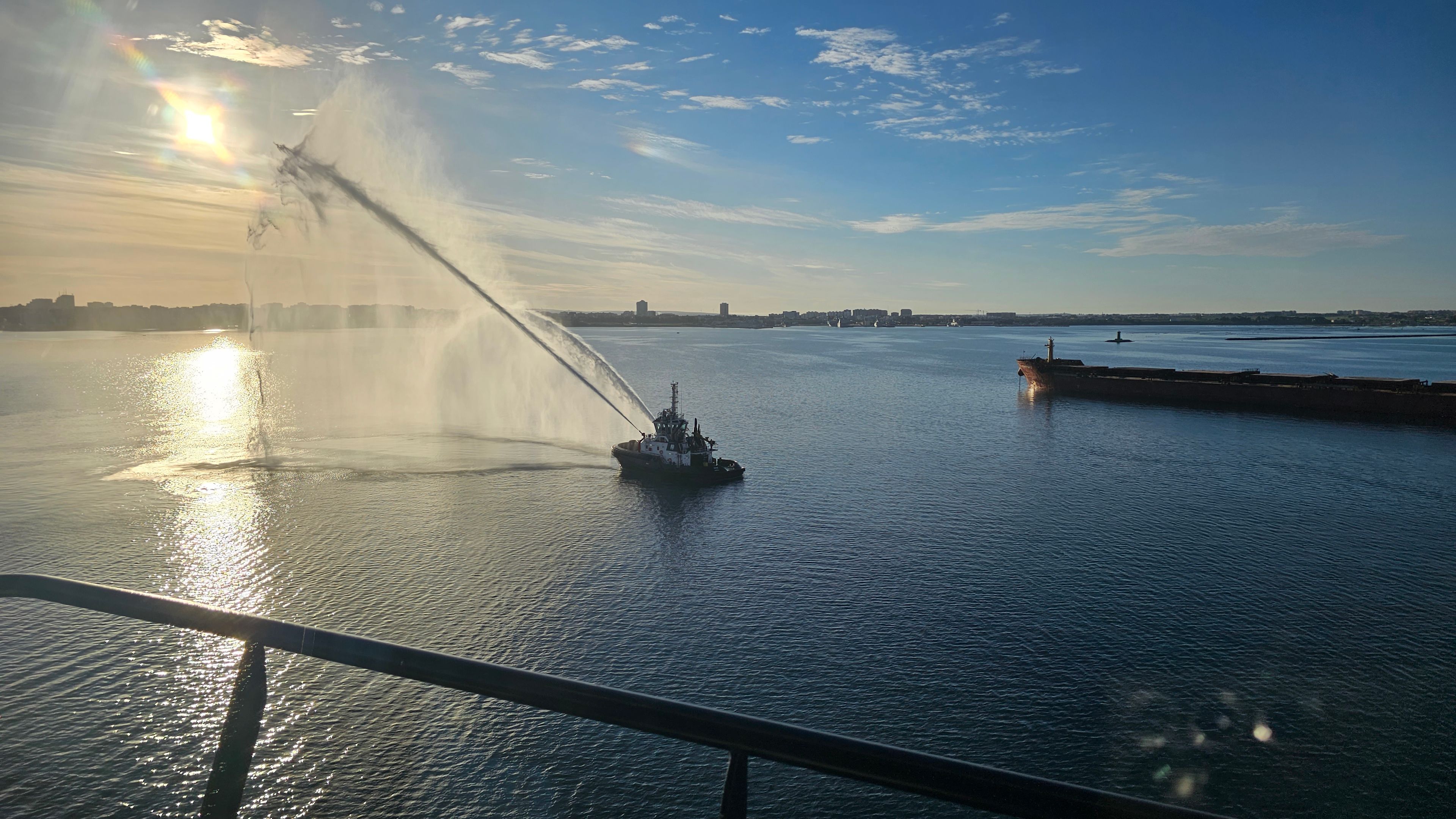 Schlepper sprüht Wasser im Hafen bei Sonnenuntergang, Frachtschiff im Hintergrund. Schlepper sprüht Wasser im Hafen bei Sonnenuntergang, Frachtschiff im Hintergrund.