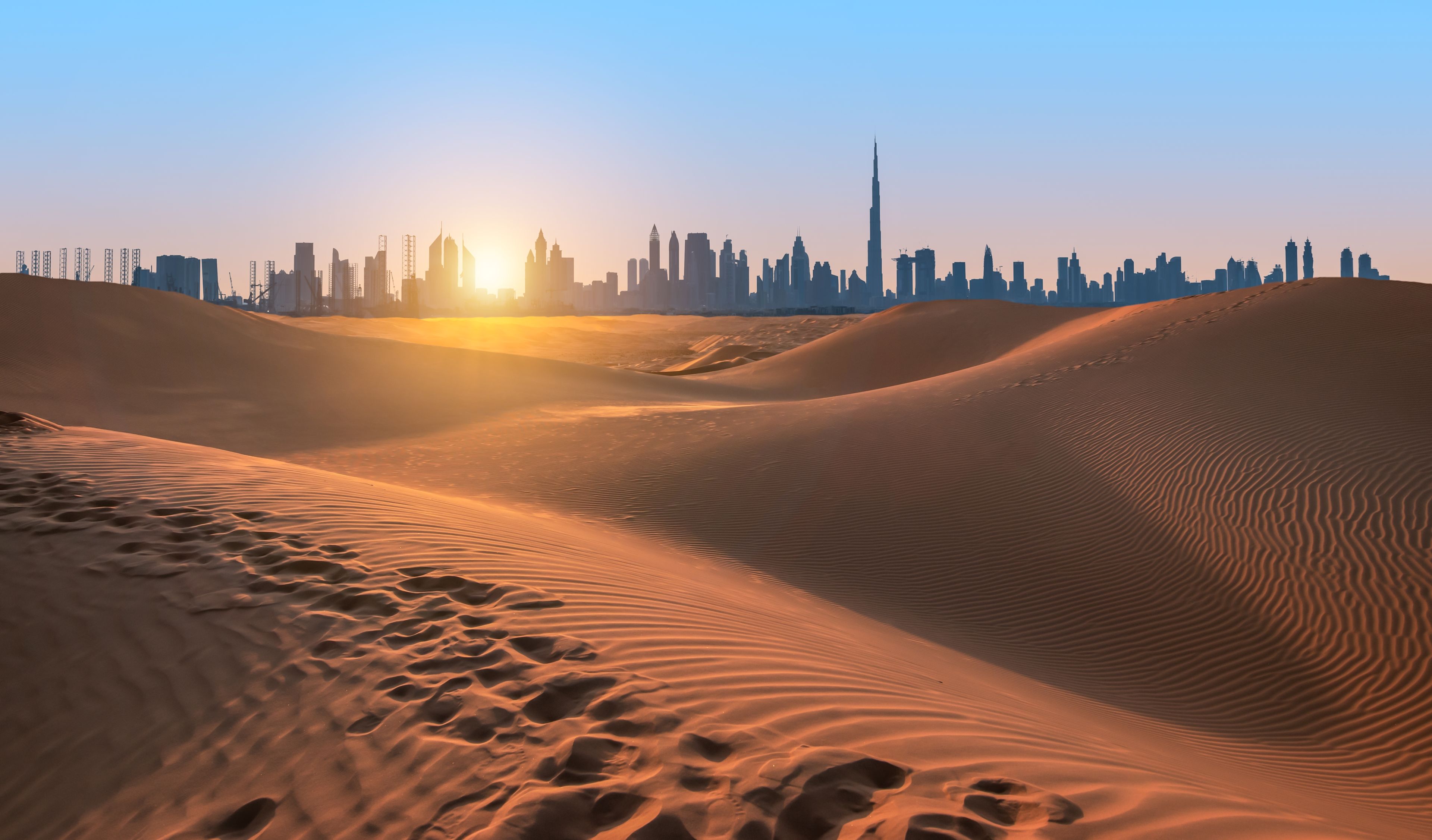 Wüstenlandschaft bei Sonnenuntergang, Dubai Skyline im Hintergrund.
