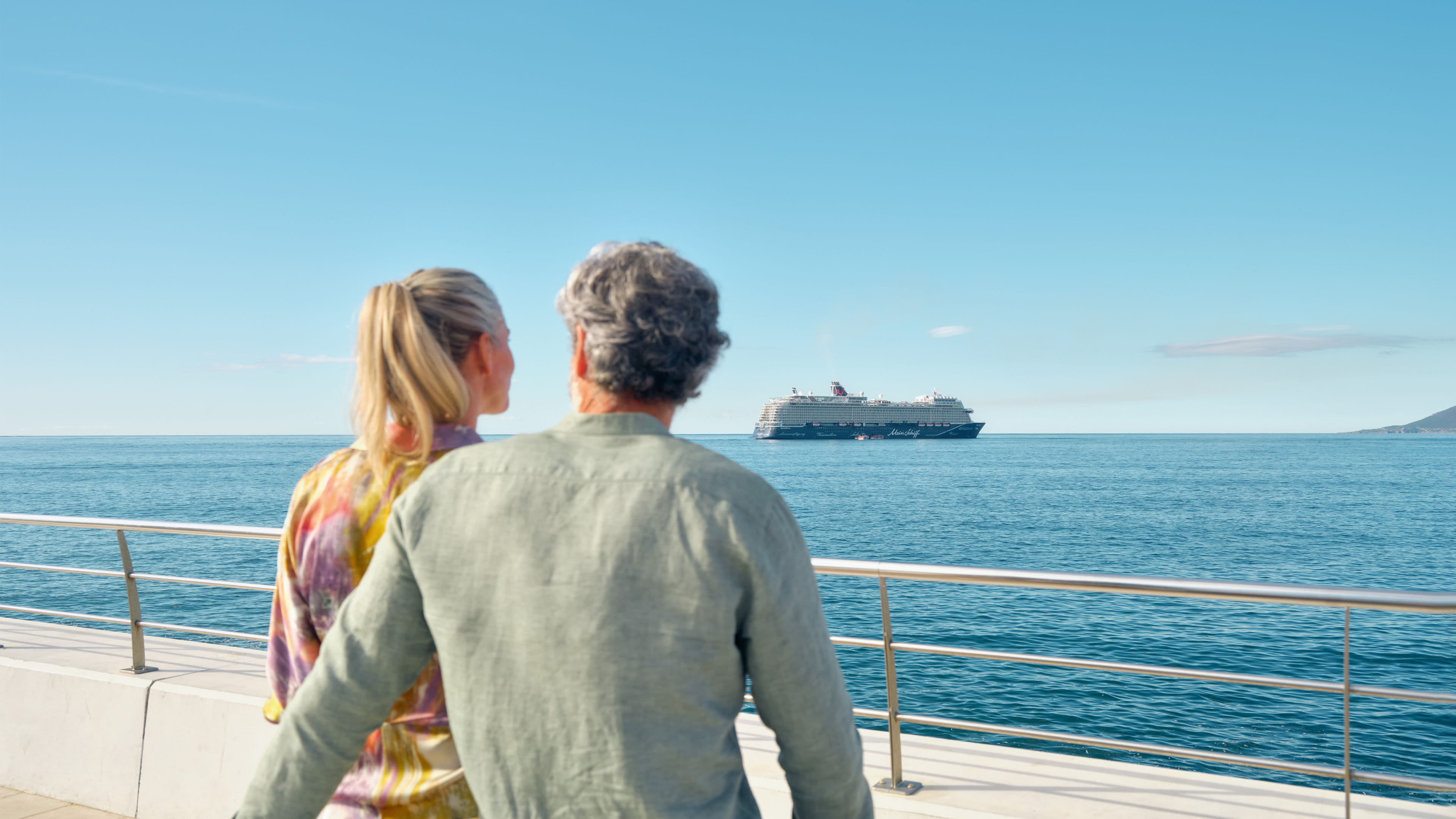 Paar blickt auf Kreuzfahrtschiff der Mein Schiff® Flotte im Meer.