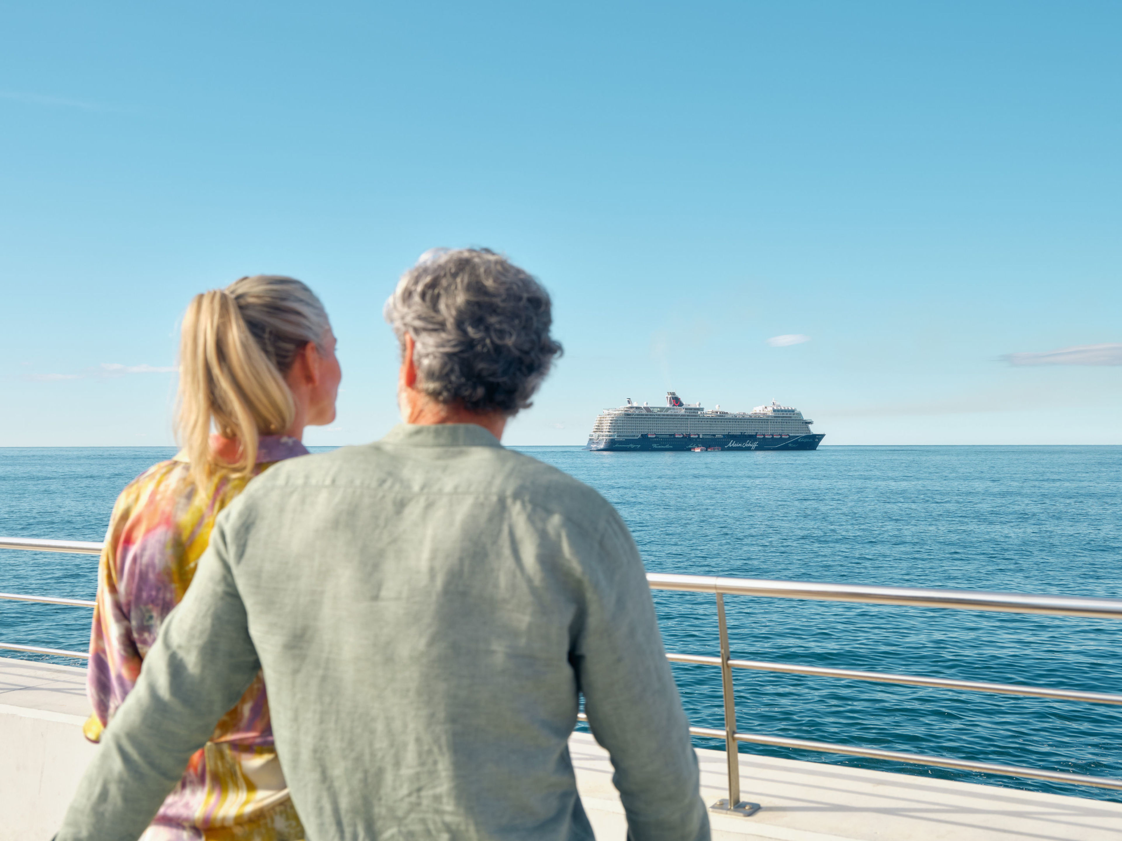 Paar blickt auf Kreuzfahrtschiff der Mein Schiff® Flotte im Meer. Paar blickt auf Kreuzfahrtschiff der Mein Schiff® Flotte im Meer.