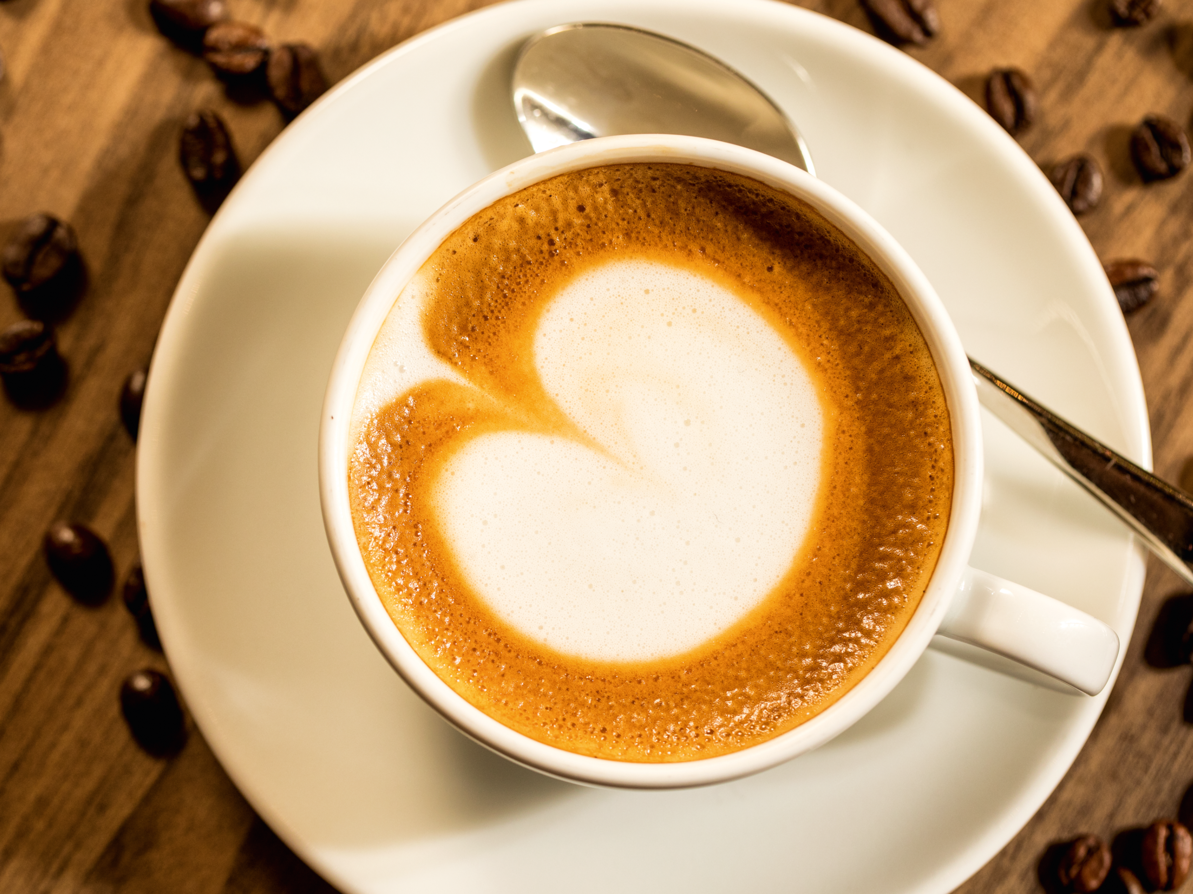 Cappuccino mit Herzmuster, Kaffeebohnen auf Holztisch. Cappuccino mit Herzmuster, Kaffeebohnen auf Holztisch.