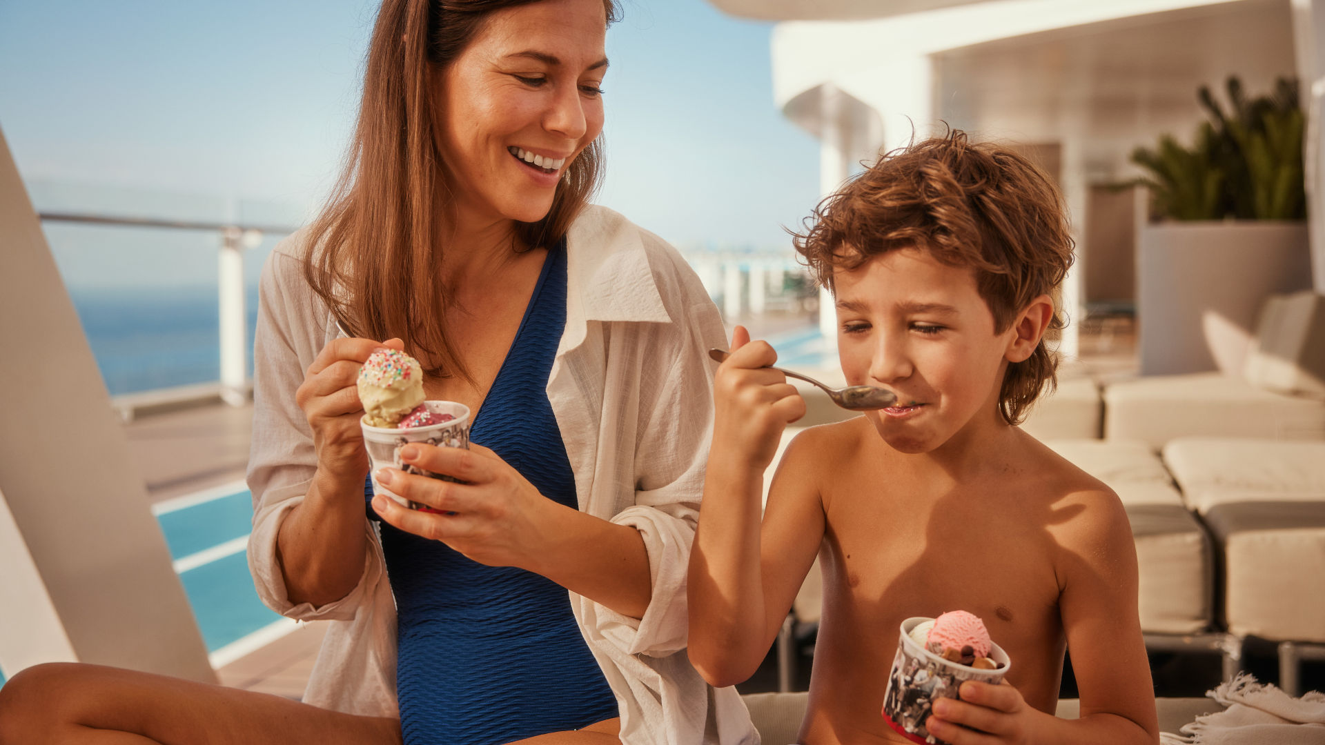Frau und Kind essen Eis mit Meerblick, sonniger Tag.