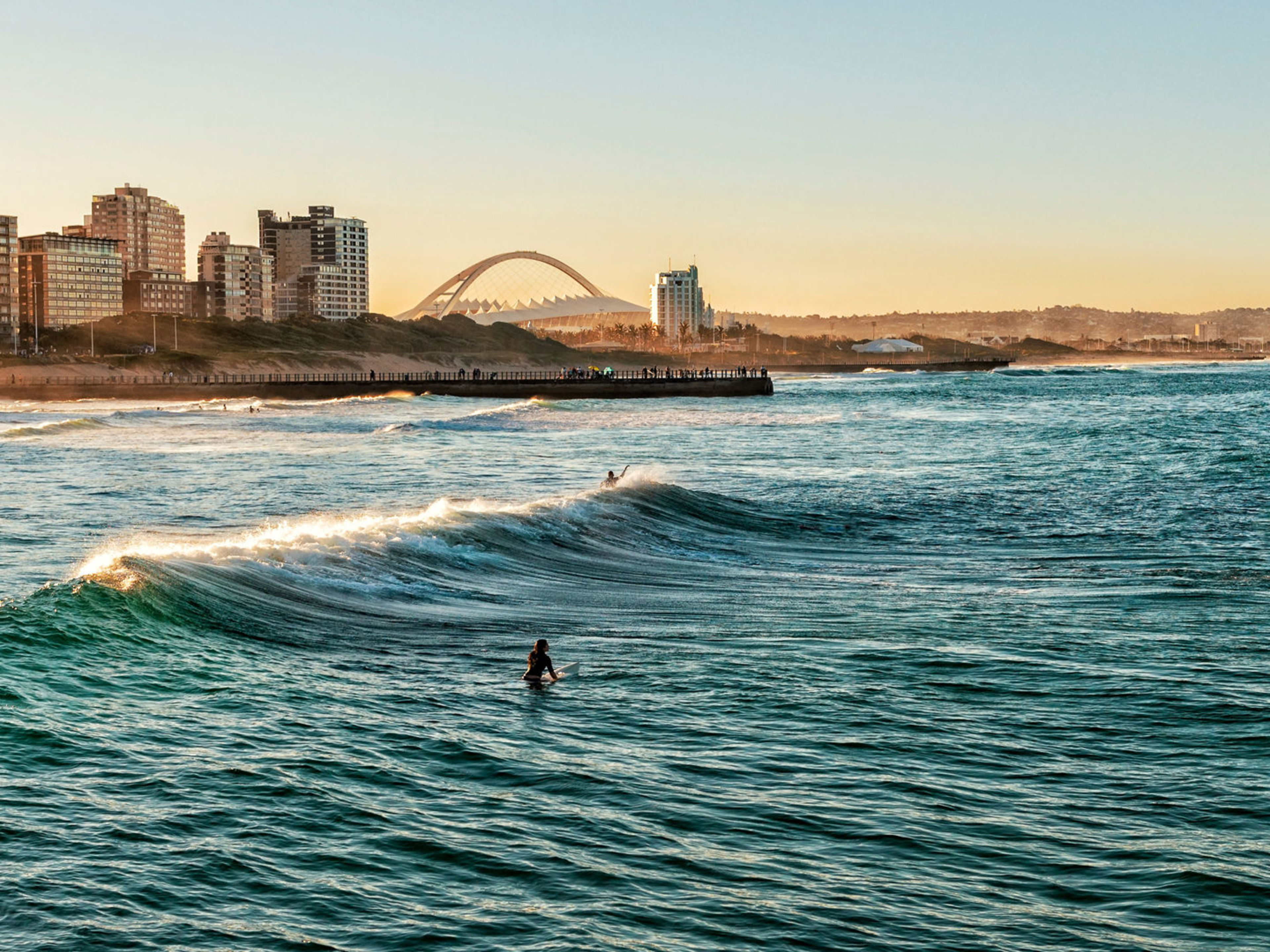 Surfer auf Wellen vor Durban Skyline bei Sonnenuntergang. Surfer auf Wellen vor Durban Skyline bei Sonnenuntergang.