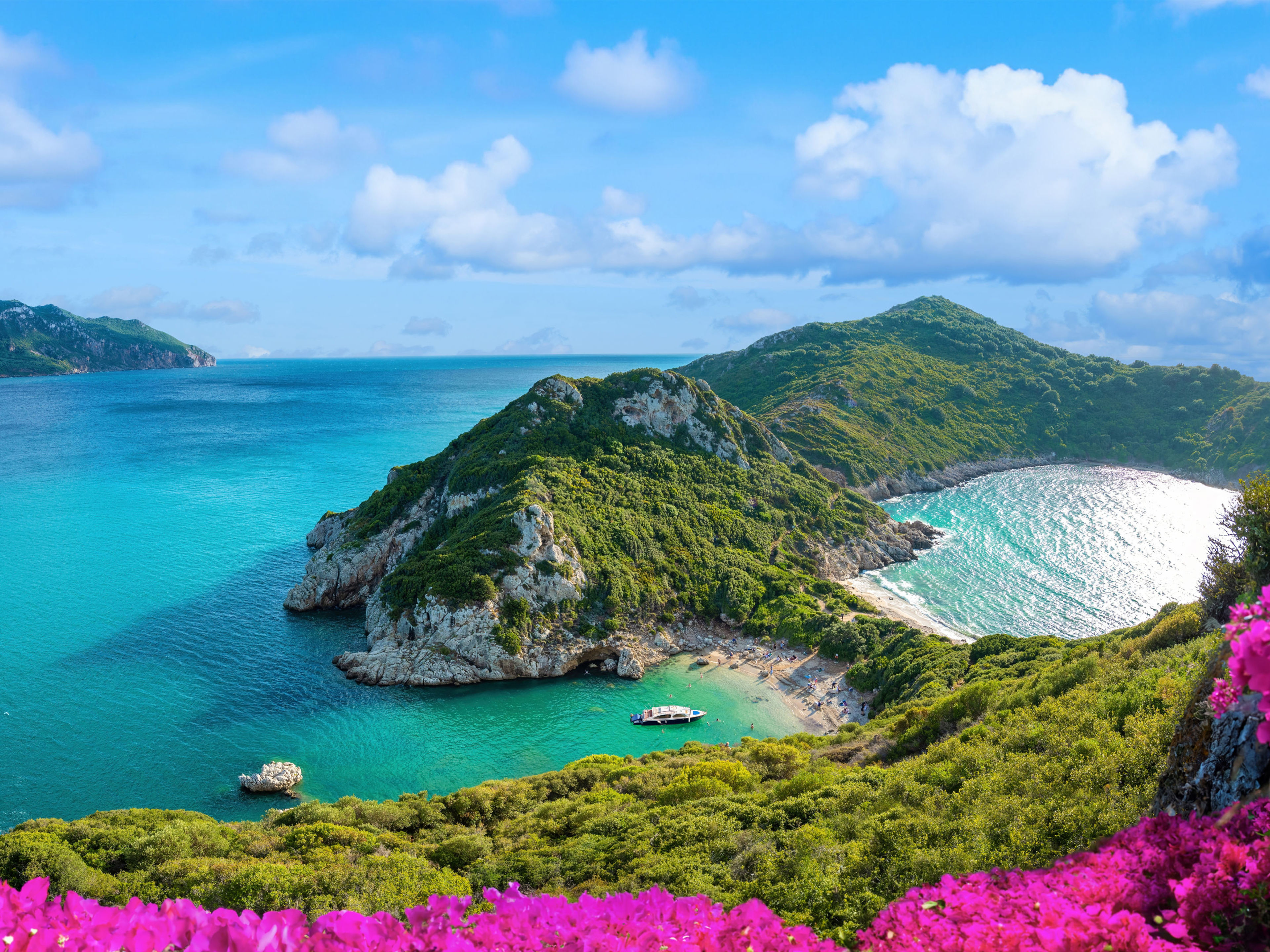 Küste von Korfu mit türkisfarbenem Meer, grünen Hügeln und pinken Blumen. Küste von Korfu mit türkisfarbenem Meer, grünen Hügeln und pinken Blumen.