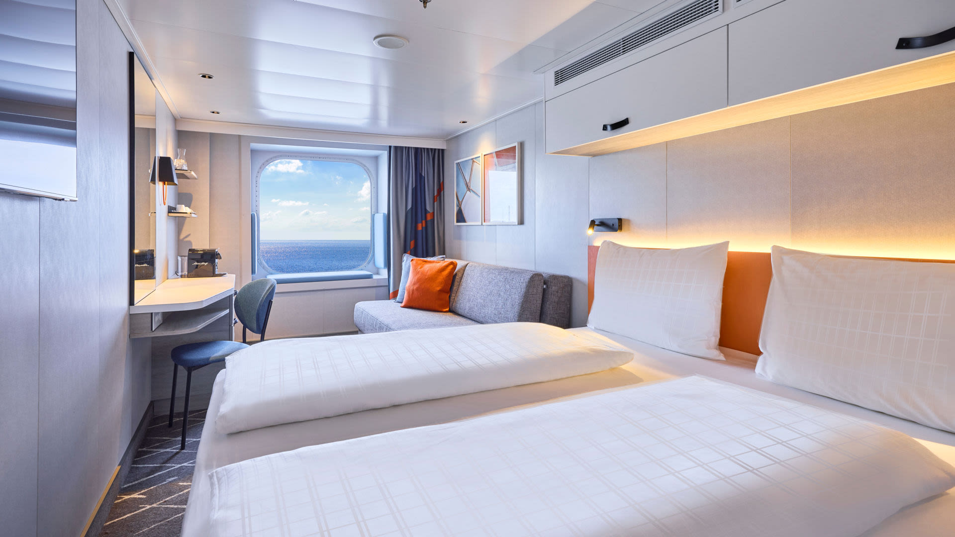 Helles Kreuzfahrtschiff-Kabine mit Meerblick, Doppelbett, Sofa, Schreibtisch.