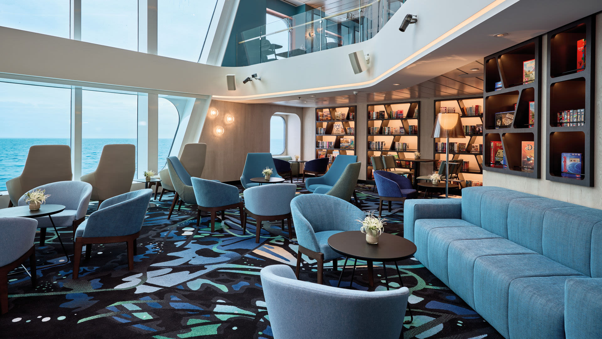 Moderne Lounge auf Kreuzfahrtschiff mit blauen Sesseln und Meerblick.